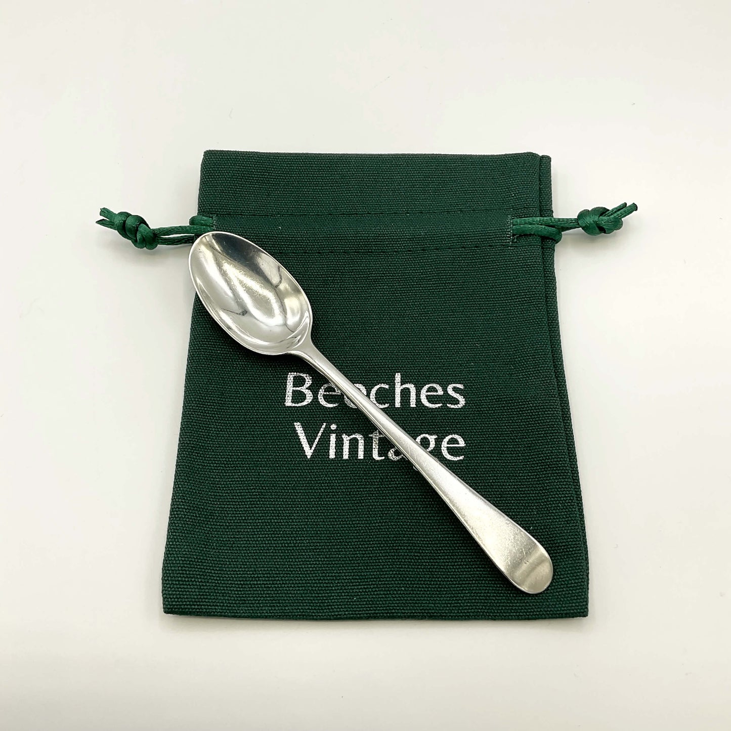 Antique silver coffee spoon sitting on a green gift bag on a white background 