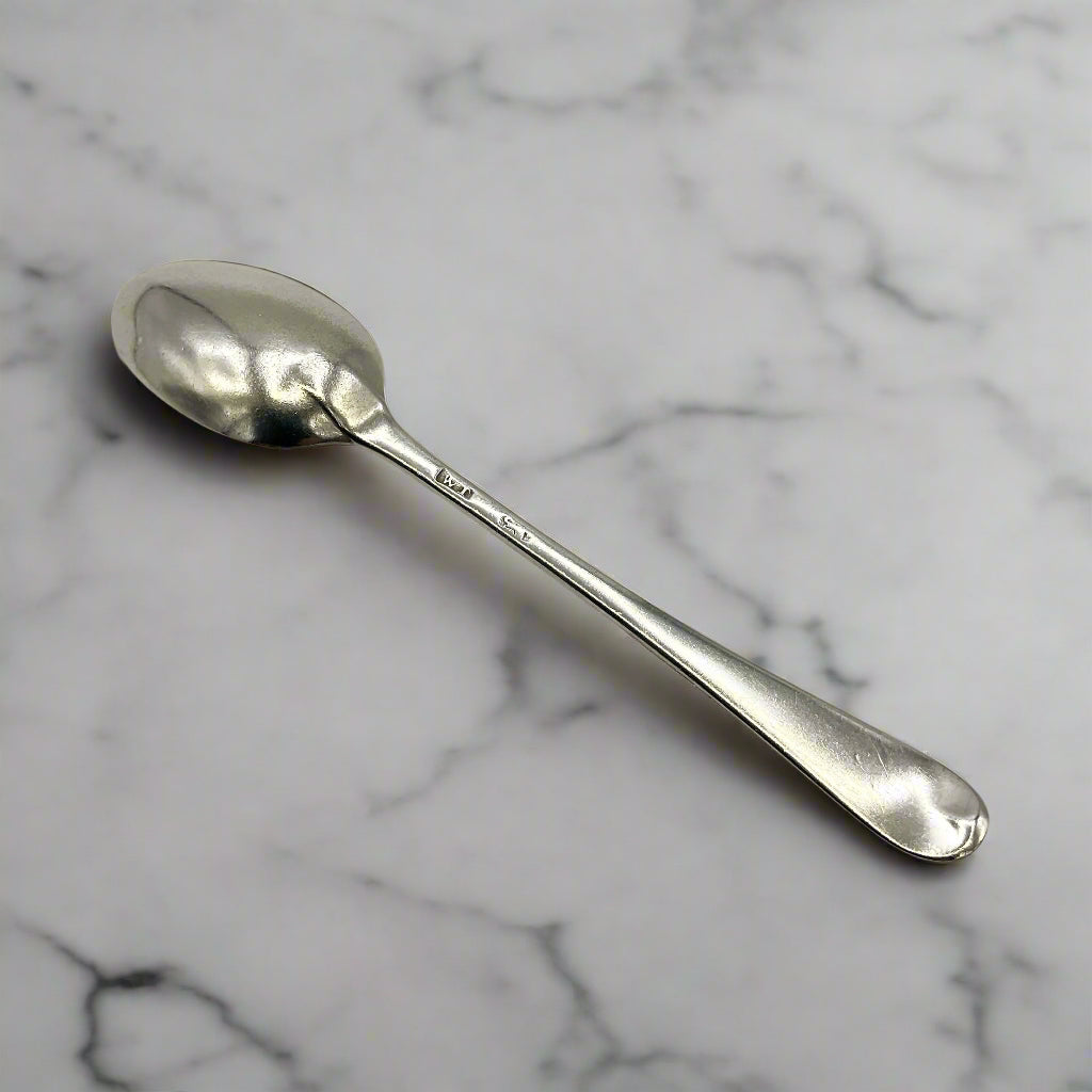 Back of Antique silver coffee spoon on a white marble workbench