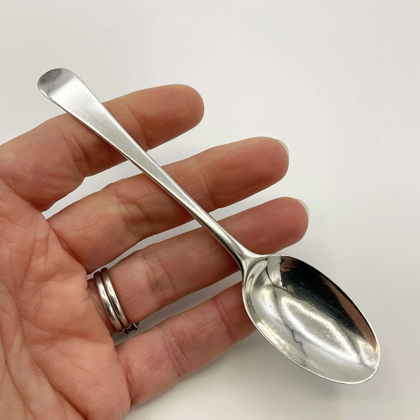 Antique silver coffee spoon held in a hand on a white background 