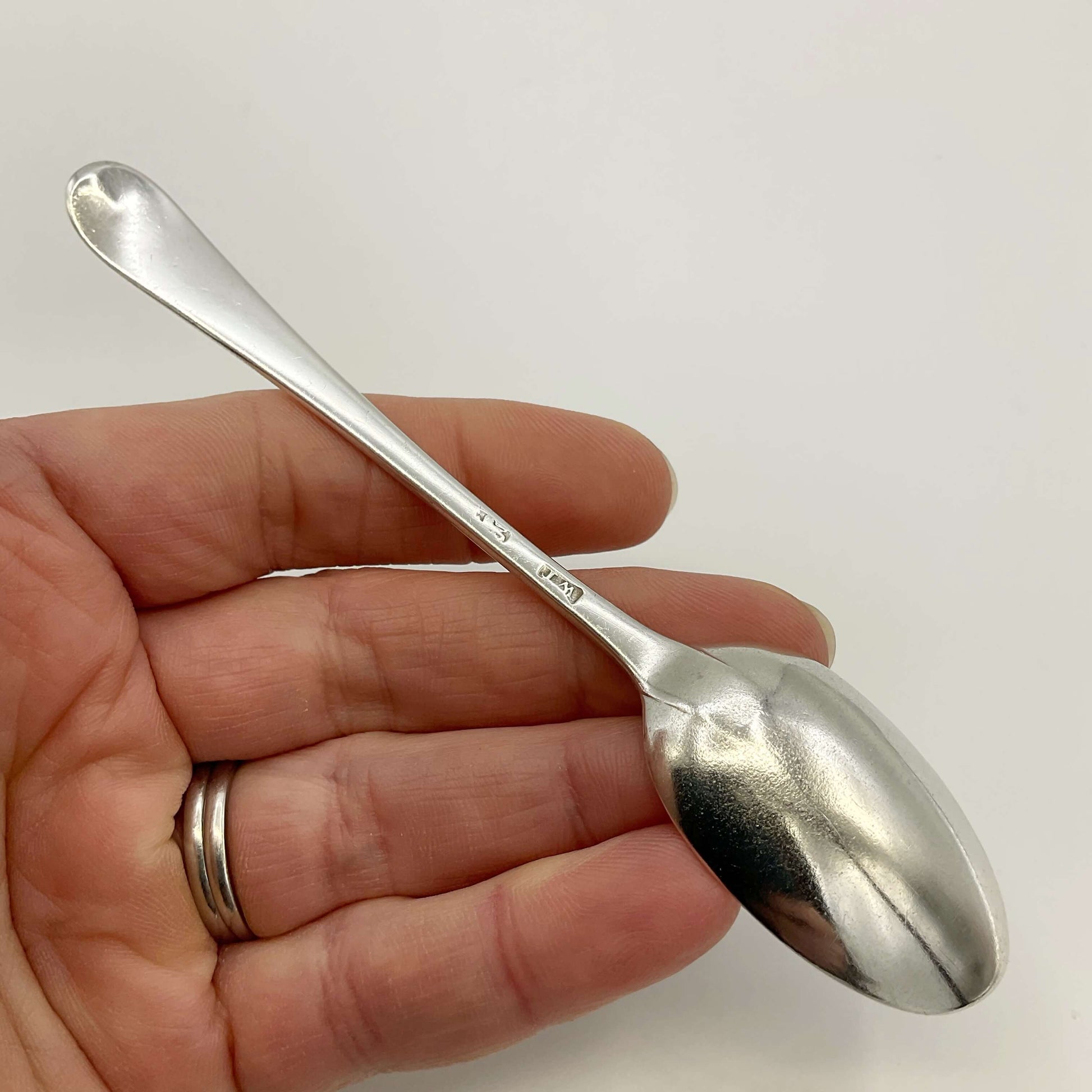 Back of antique silver coffee spoon held in a hand on a white background 