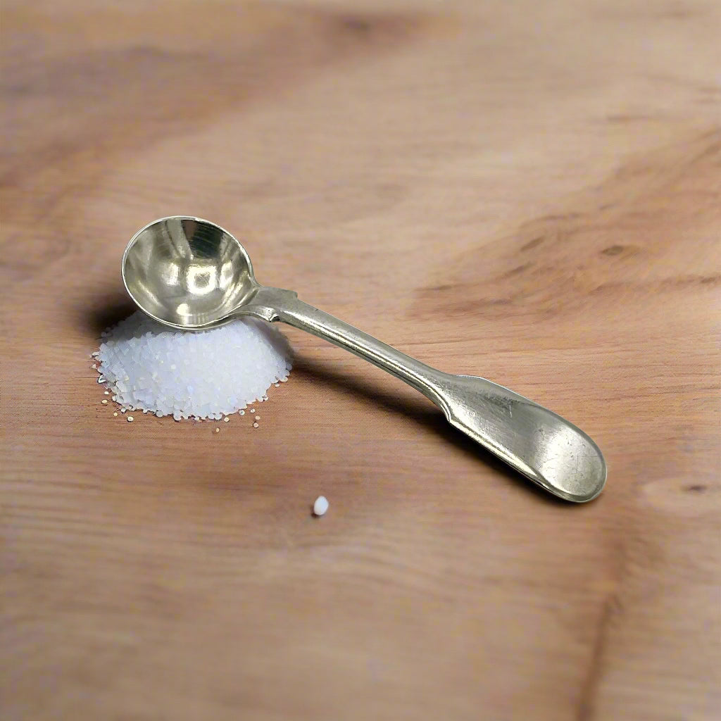 Antique silver salt spoon on a pile of salt on a wood table