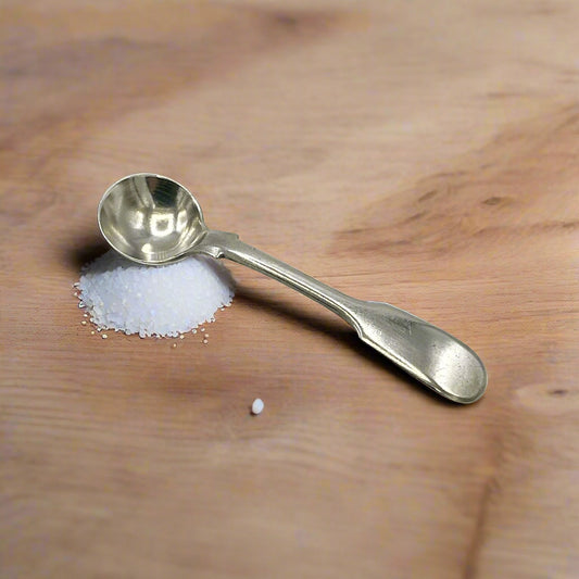 Antique silver salt spoon on a pile of salt on a wood table
