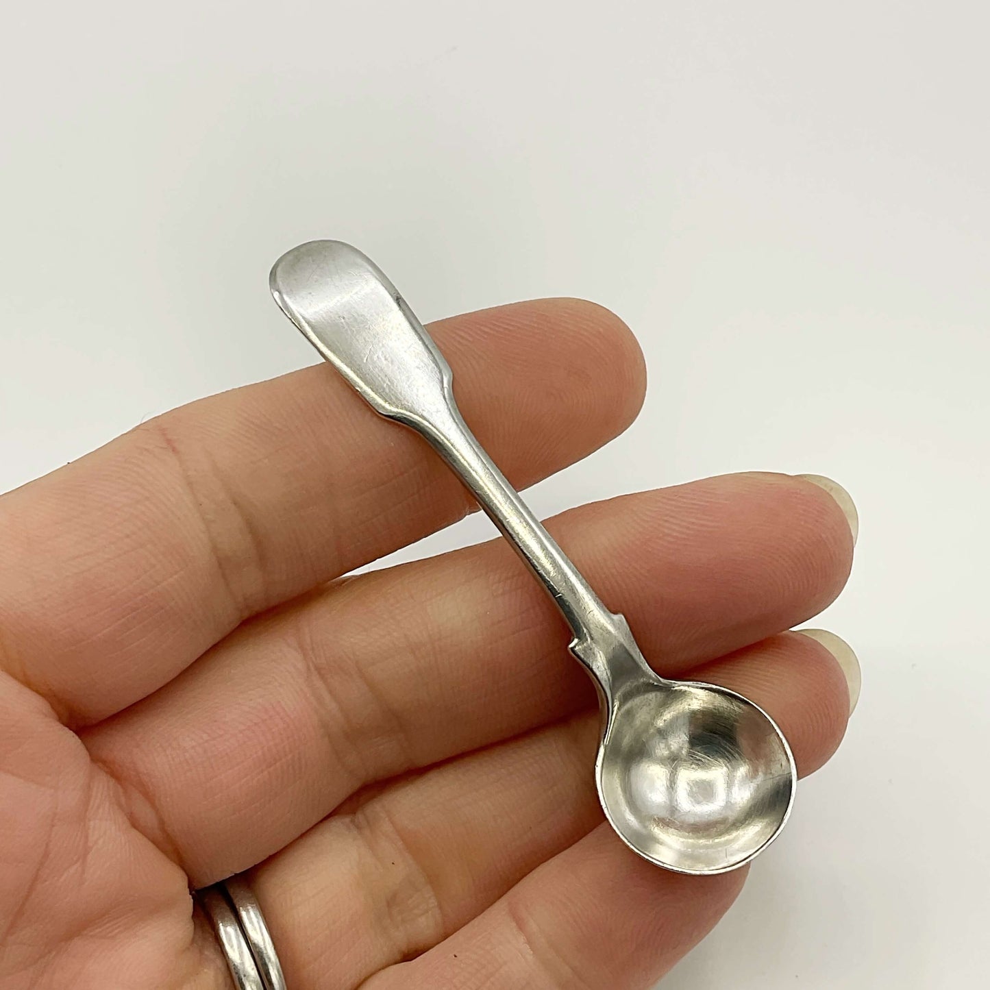 Antique silver salt spoon held in a hand on a white background 