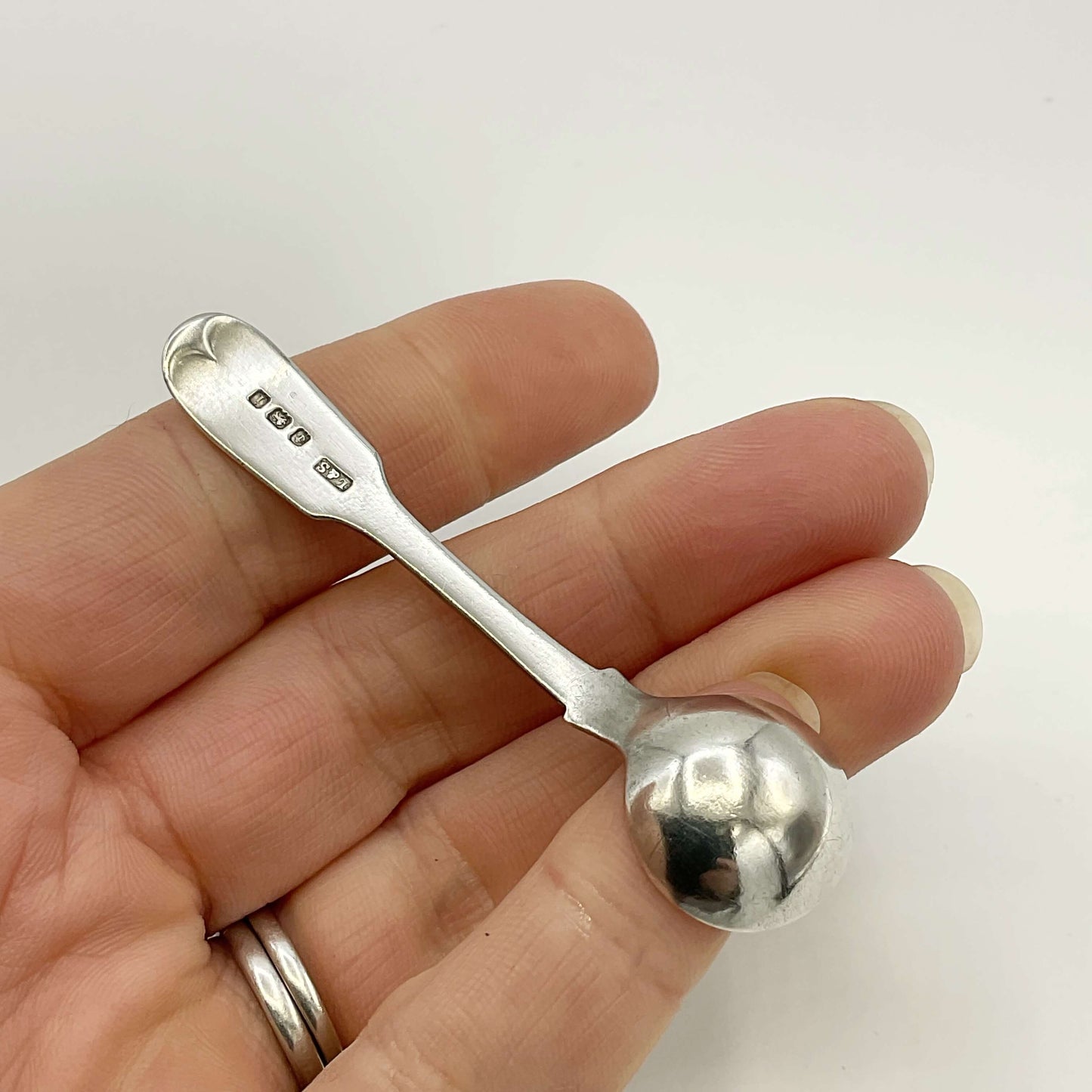 Back of Antique silver salt spoon held in a hand on a white background 