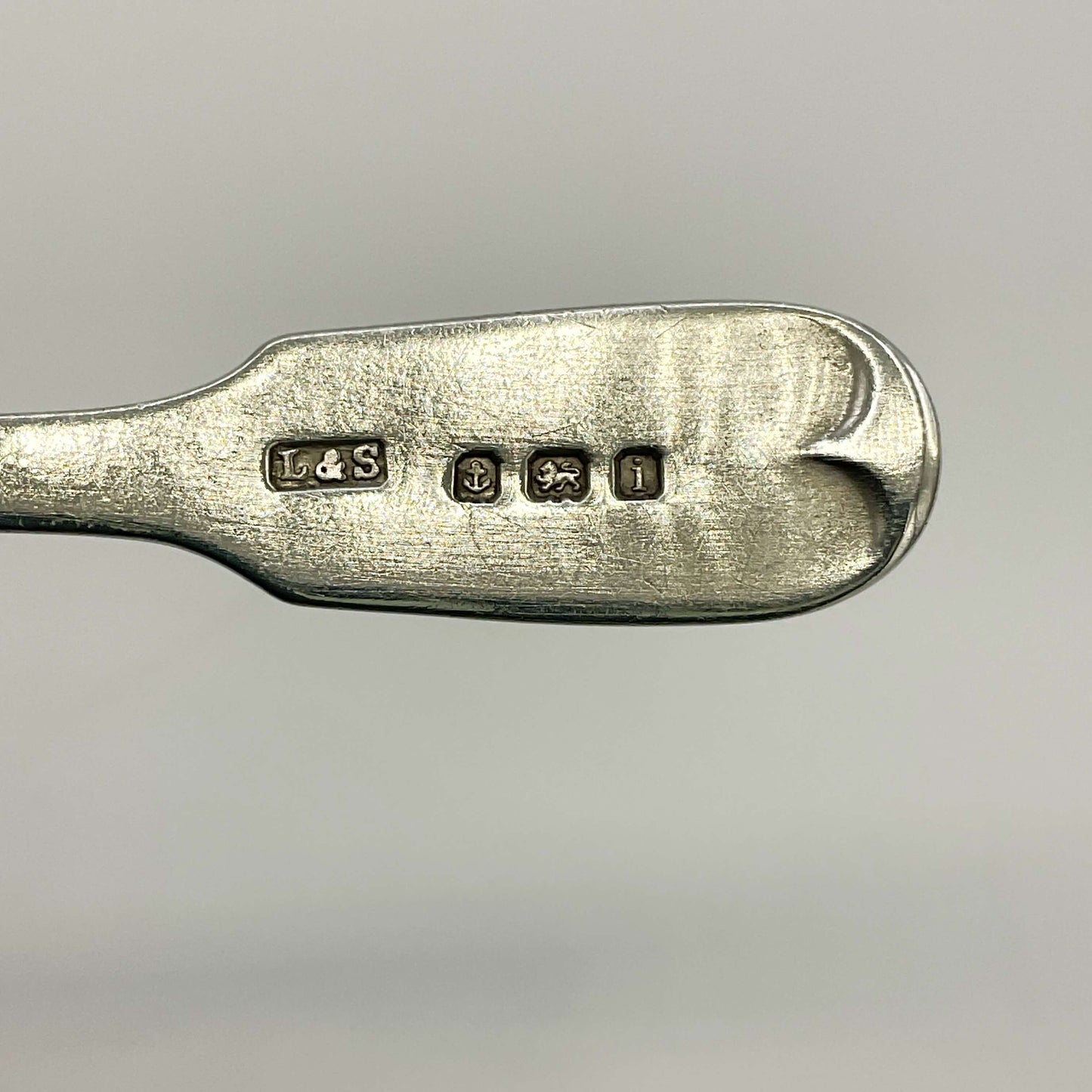 The hallmarks on the back of a spoon handle with a white background 