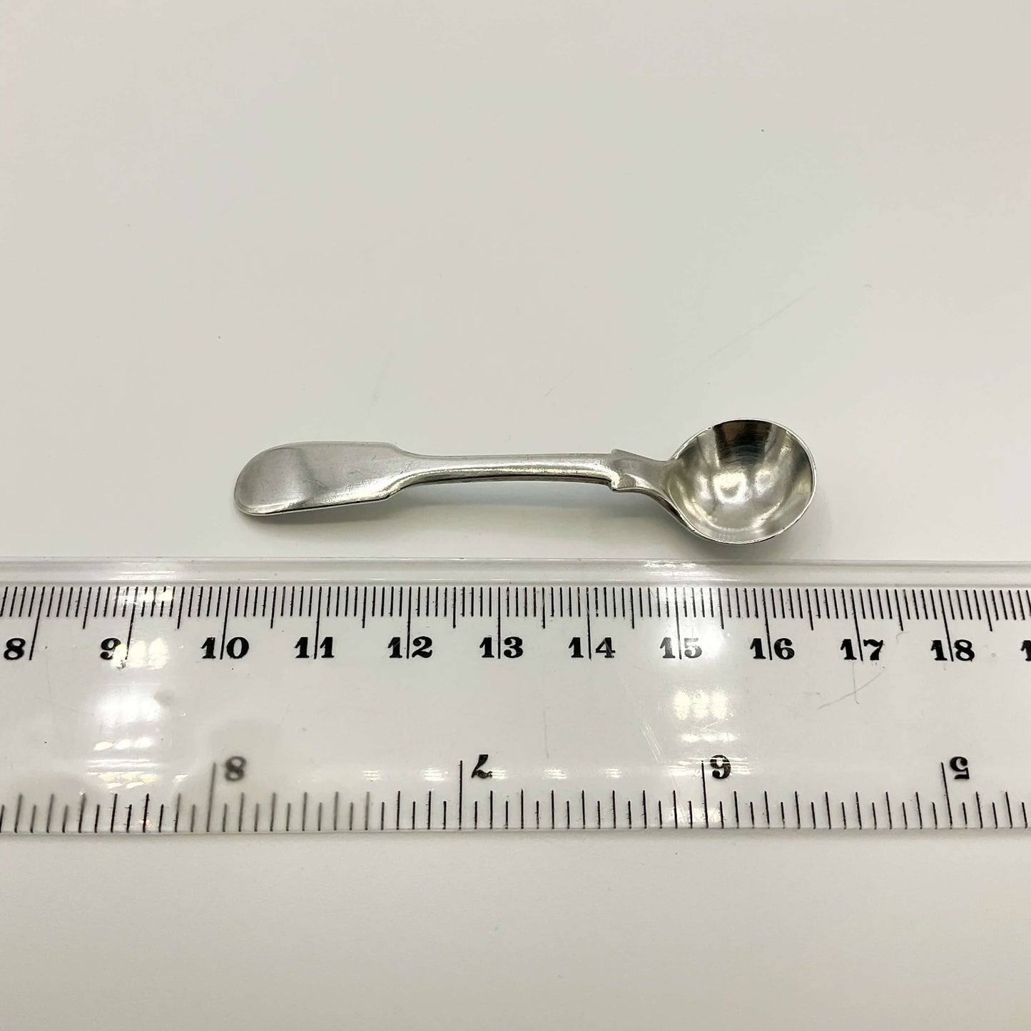 Antique silver salt spoon next to a ruler on a white background showing the length as 6.7cm