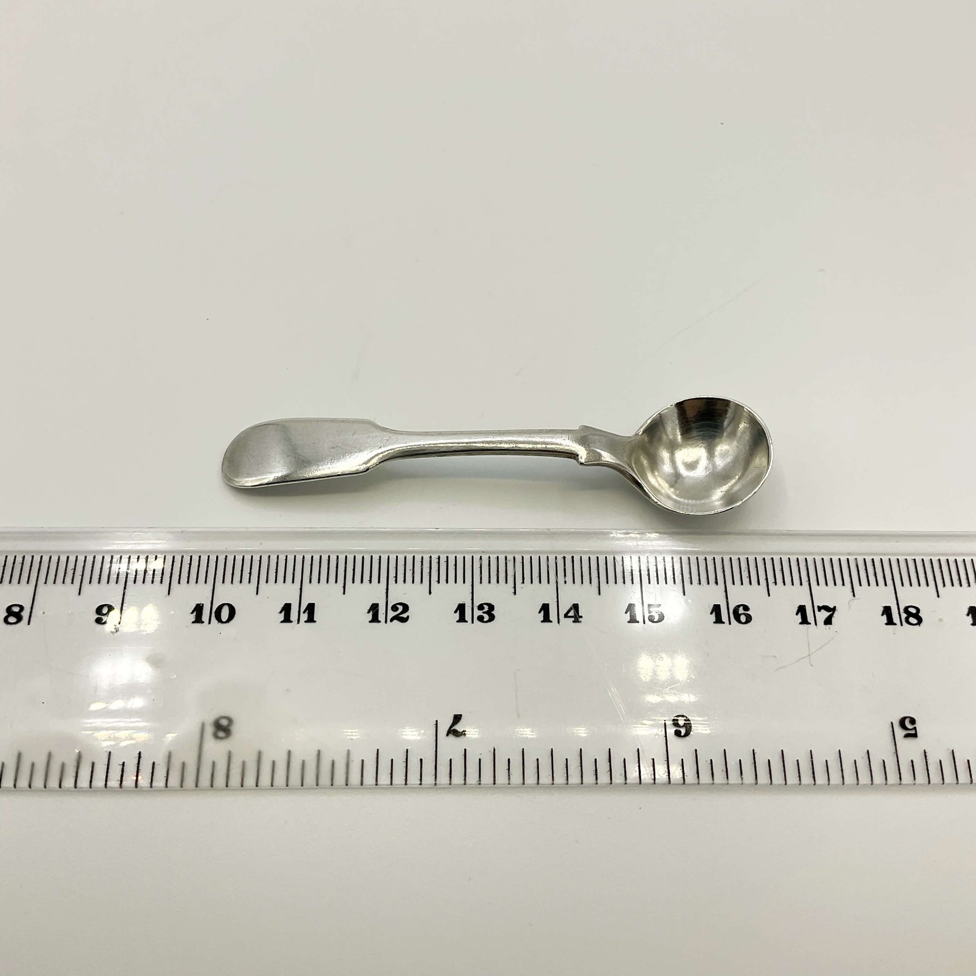 Antique silver salt spoon next to a ruler on a white background showing the length as 6.7cm