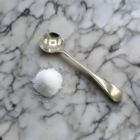 Antique silver salt spoon on a marble workbench with a pile of salt next to it
