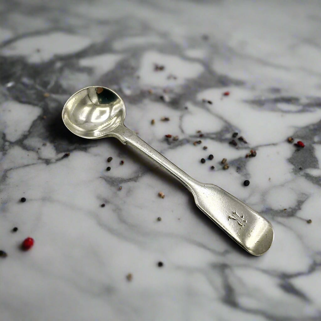 Antique silver salt spoon on a marble worktop surrounded by a few pepper grains