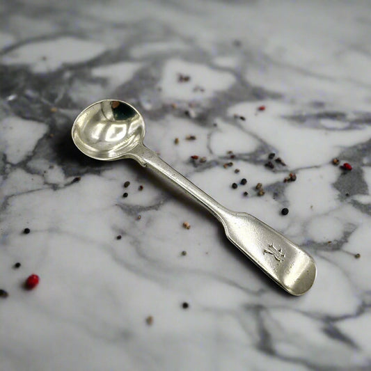 Antique silver salt spoon on a marble worktop surrounded by a few pepper grains
