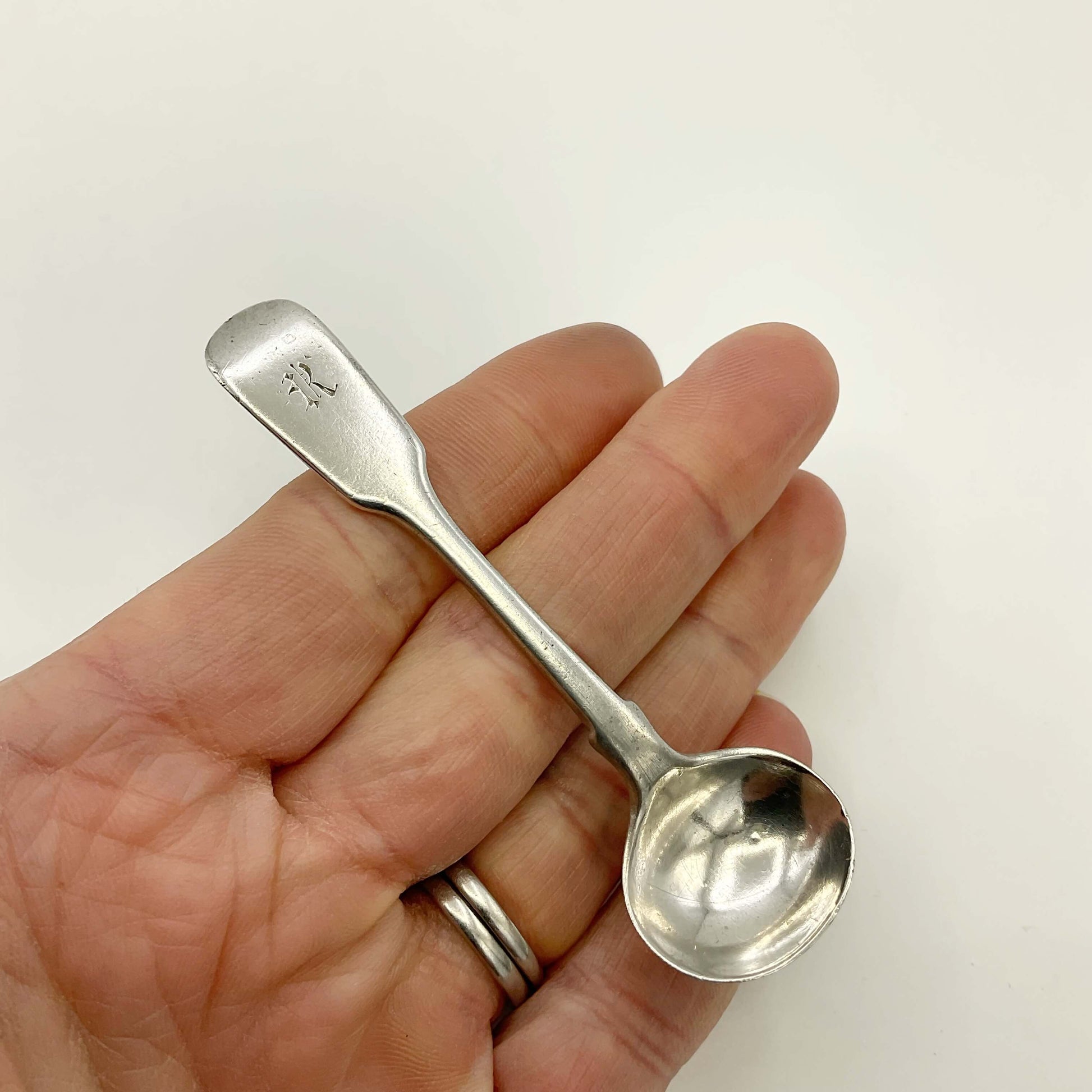 Antique silver salt spoon held in a hand on a white background 