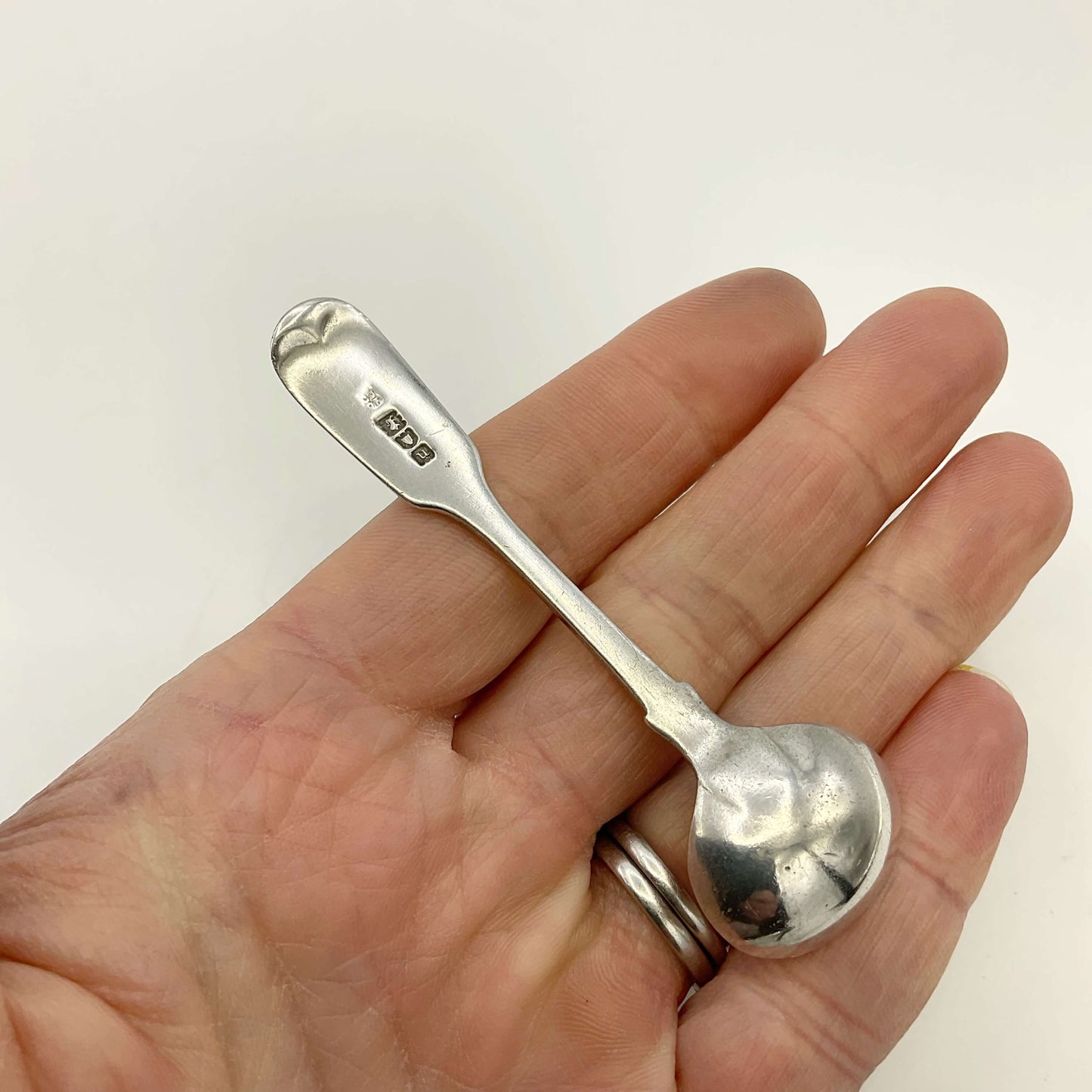 Back of Antique silver salt spoon held in a hand on a white background 