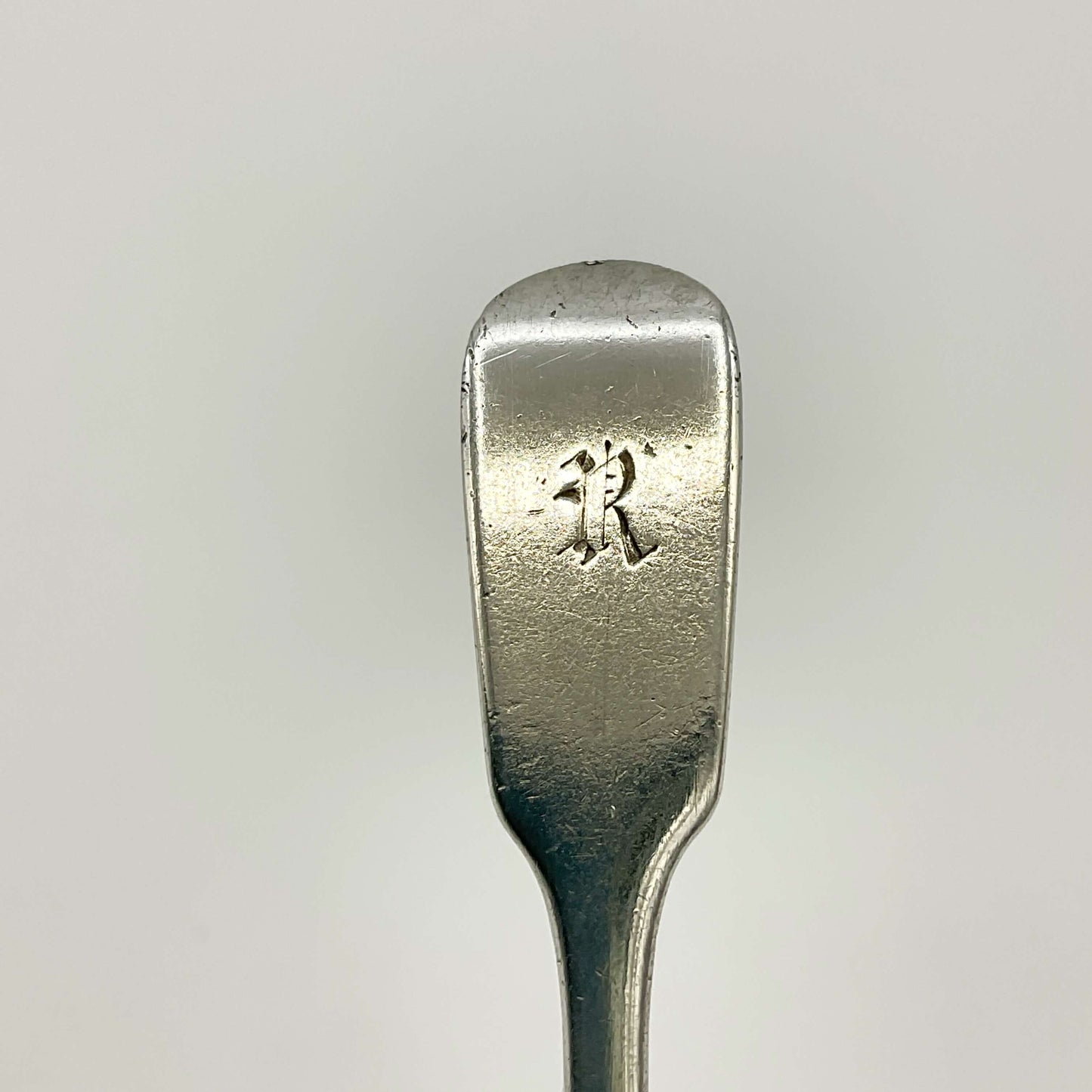 Gothic Letter R at the top of the siler spoon handle on a white background 