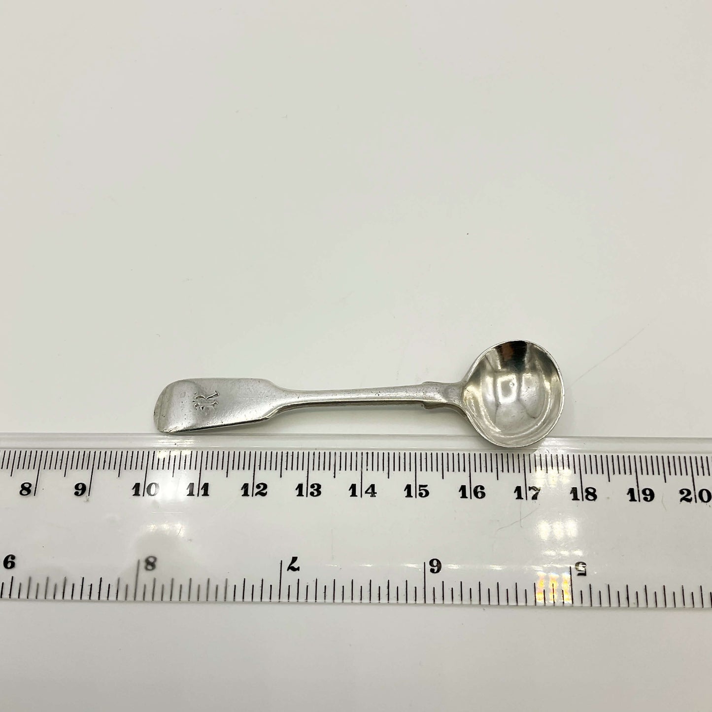 Antique silver salt spoon next to a ruler showing the length as 7.7cm  on a white background 