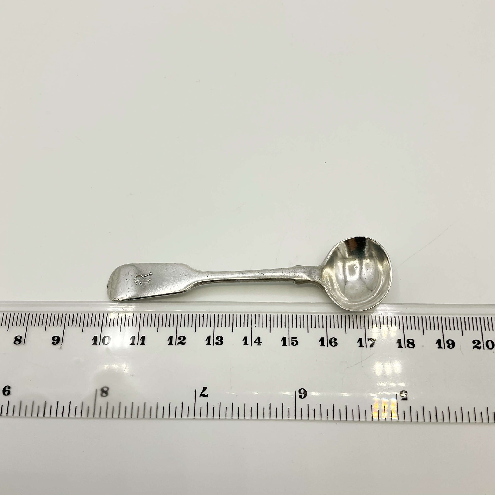 Antique silver salt spoon next to a ruler showing the length as 7.7cm  on a white background 