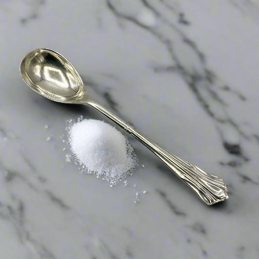 Antique salt spoon on a marble worktop next to a pile of salt