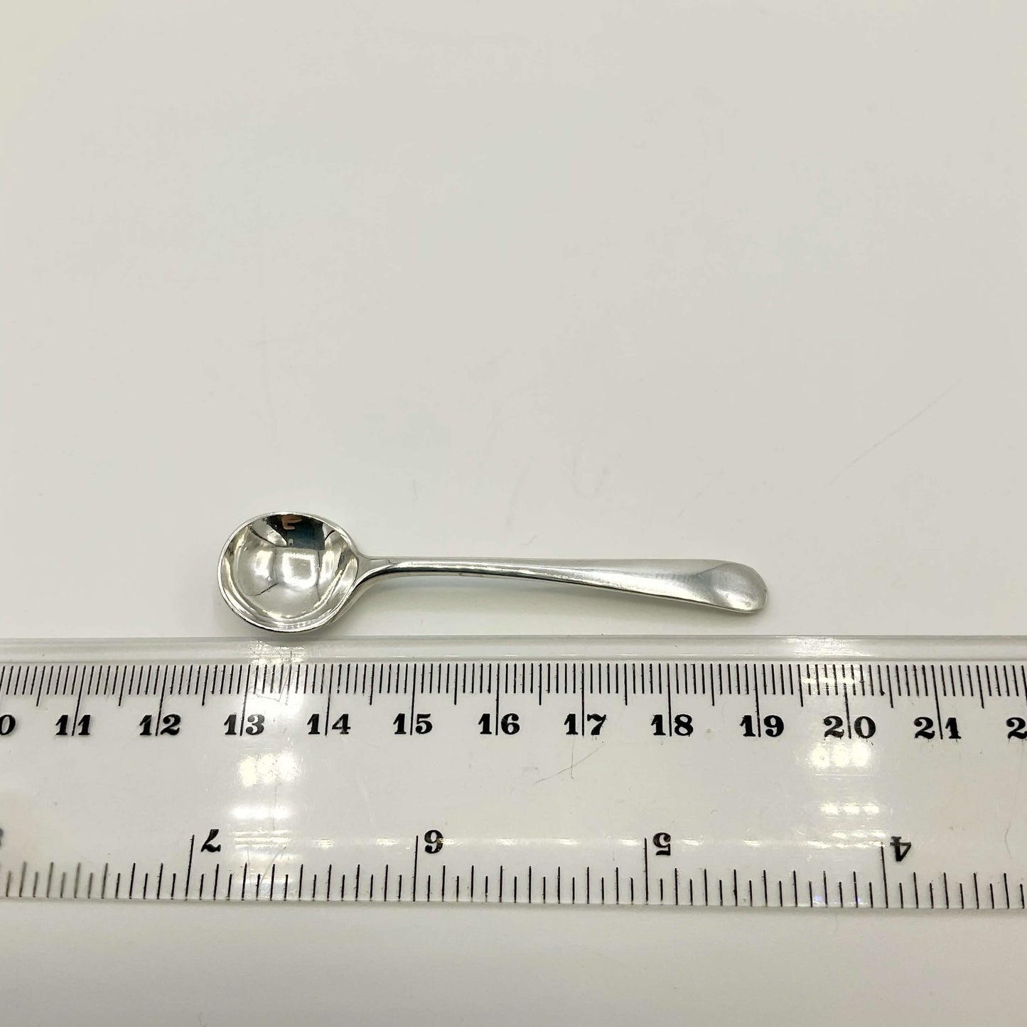 Small silver salt spoon next to a ruler on a white background showing the length as 6.6cm