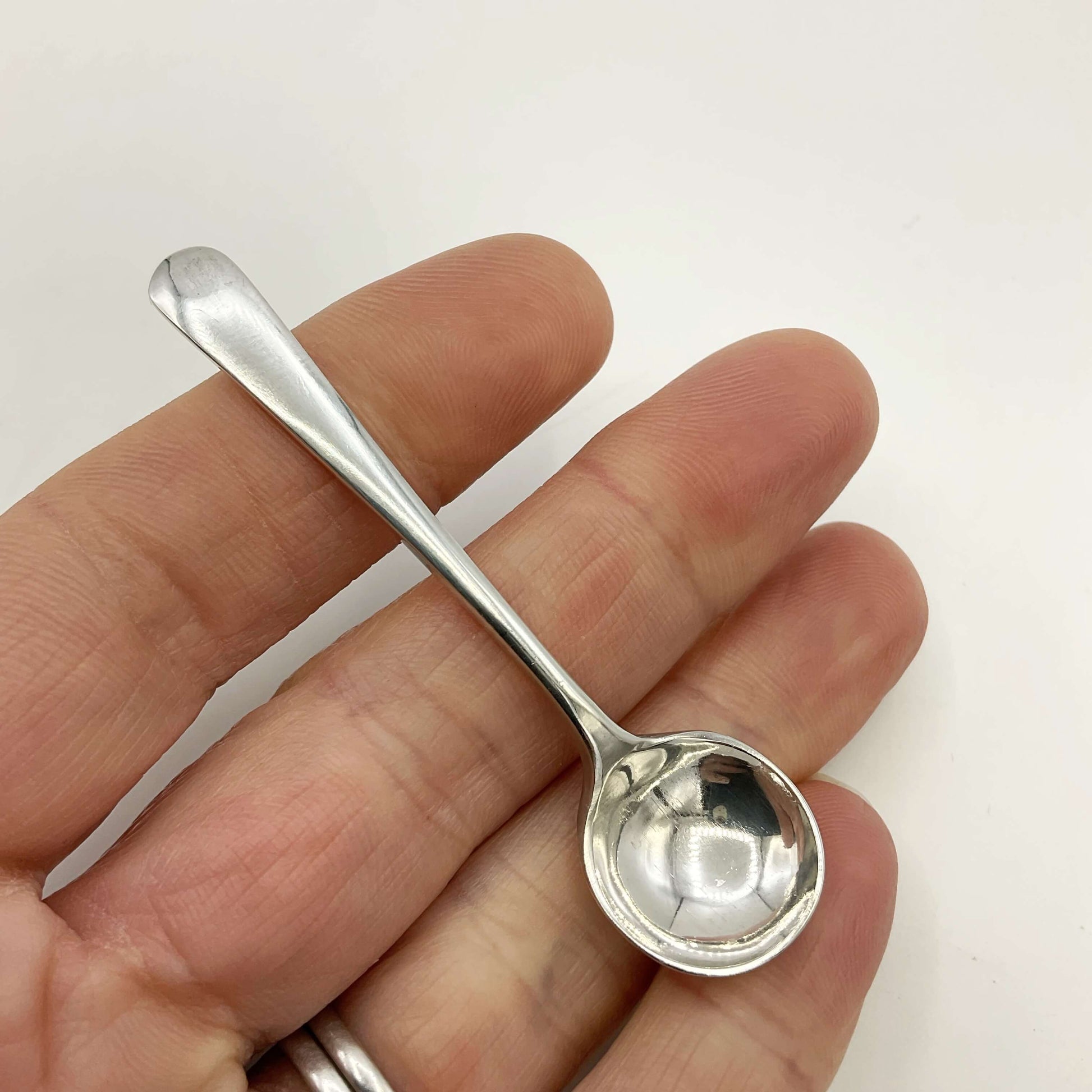Small silver salt spoon held in a hand on a white background