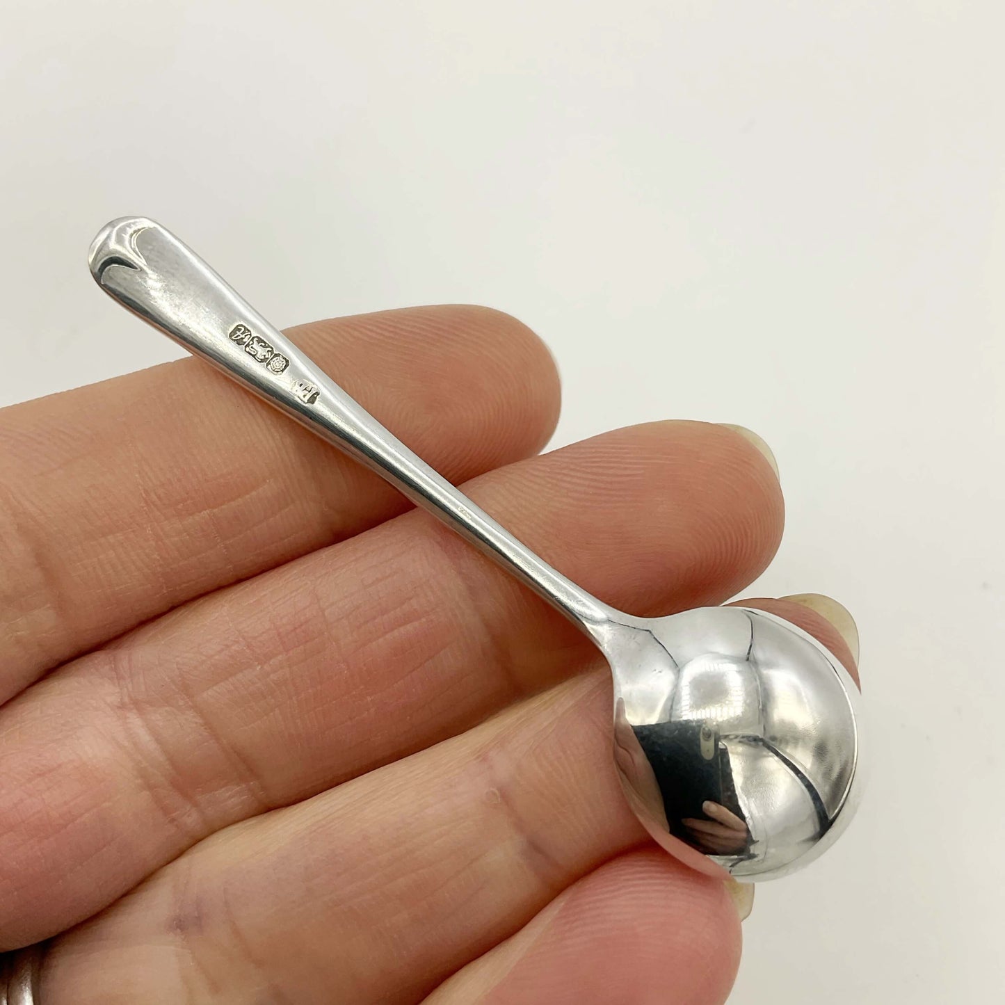 Back of a Small silver salt spoon held in a hand on a white background
