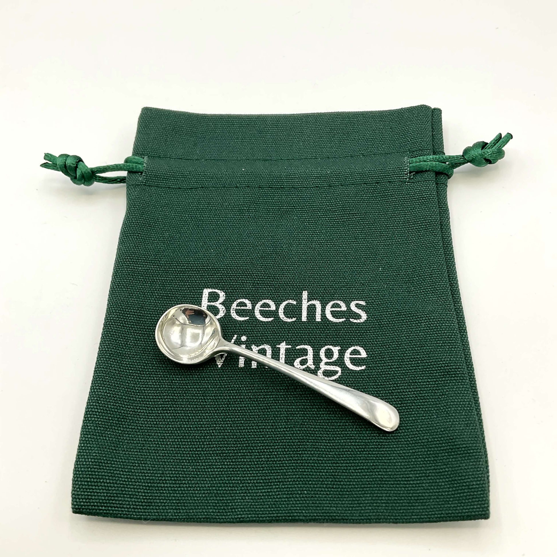 Small silver salt spoon on a green gift bag on a white background 