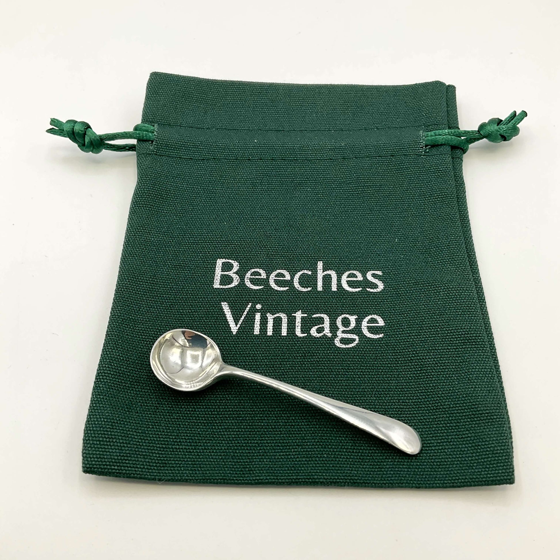 Small silver salt spoon on a green gift bag on a white background 