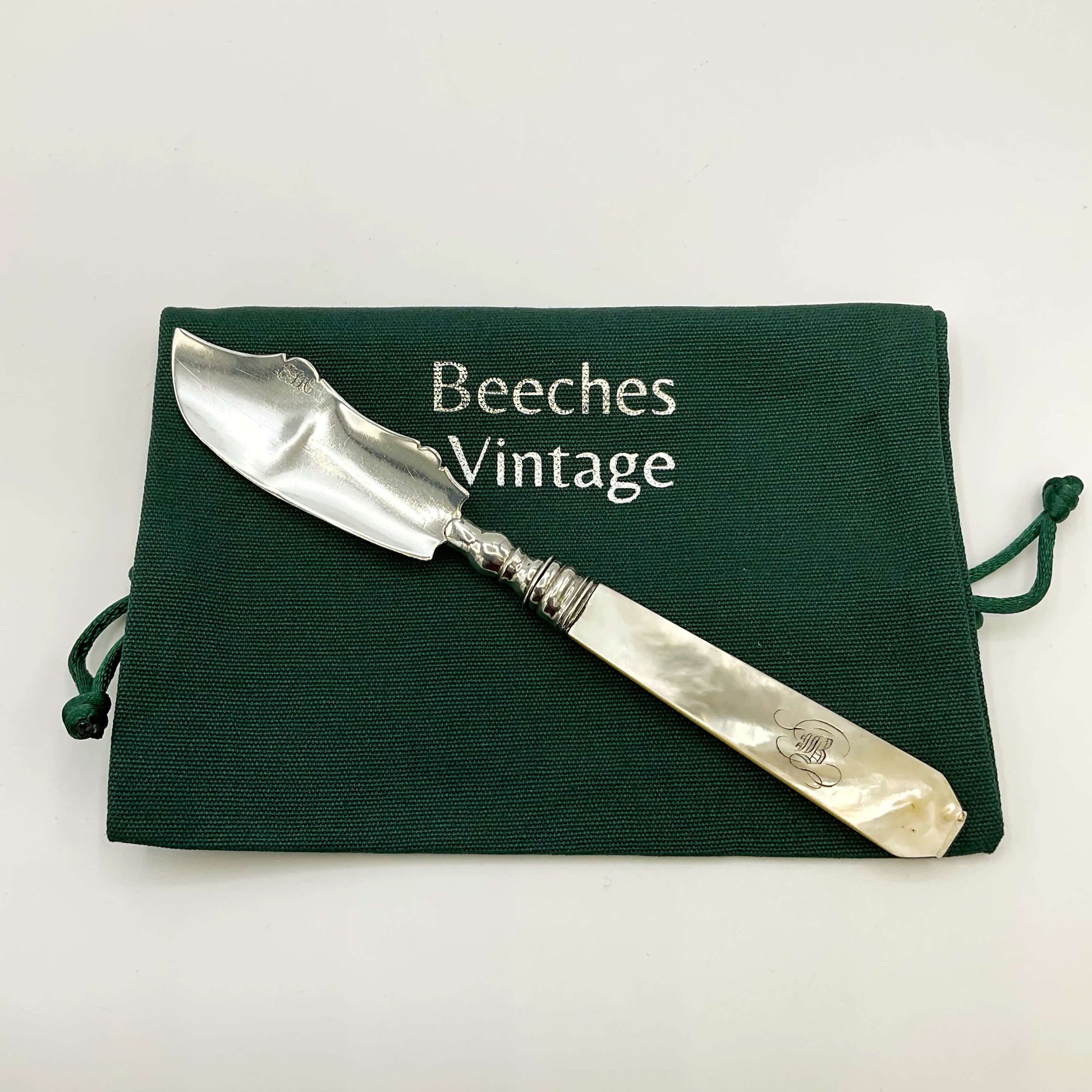 Antique silver and mother of pearl butter knife on a green gift bag and white background 
