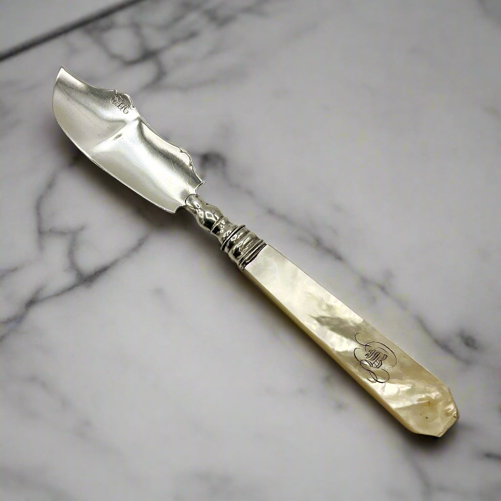 Antique silver and mother of pearl butter knife on a marble worktop