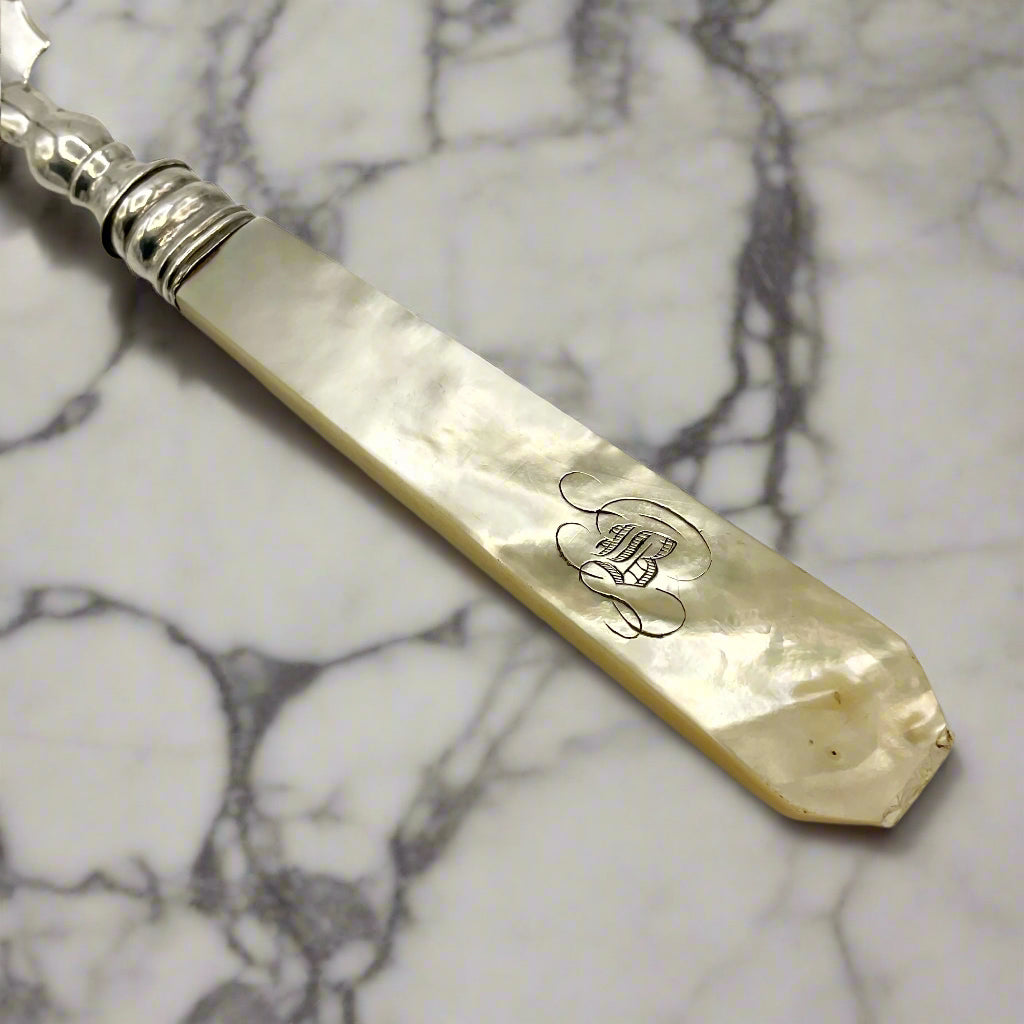 Antique silver and mother of pearl butter knife handle on a marble worktop
