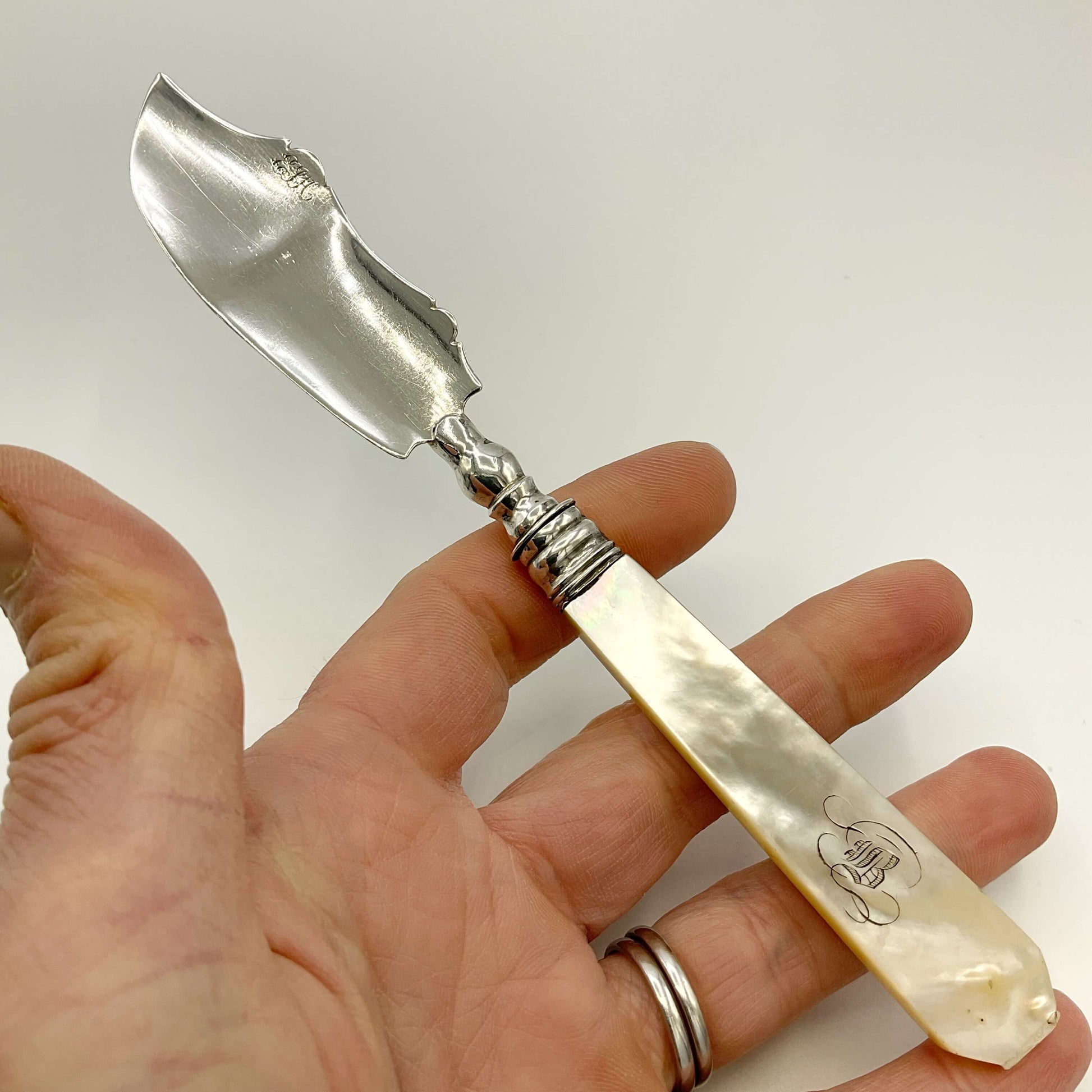 Antique silver and mother of pearl butter knife held in a hand on a white background 
