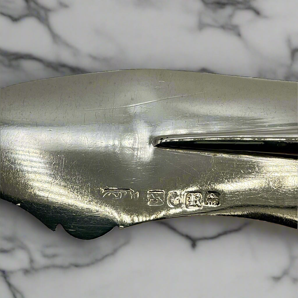 The hallmarks on the back of the antique silver butter knife blade on a marble worktop