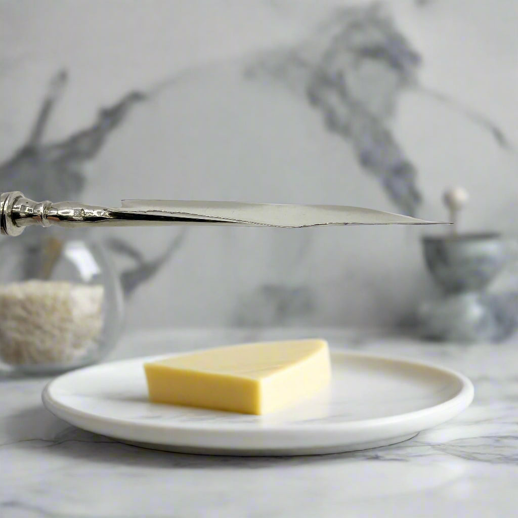 Antique butter knife blade above a pat of butter on a plate on a marble workbench