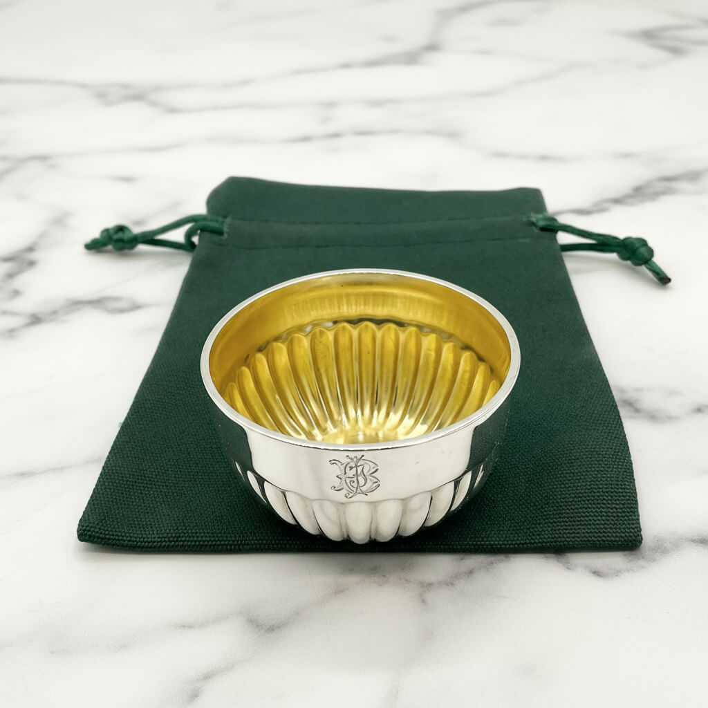 Antique sterling silver salt bowl with fluted pattern and gilded interior, displayed on a green pouch on a marble background