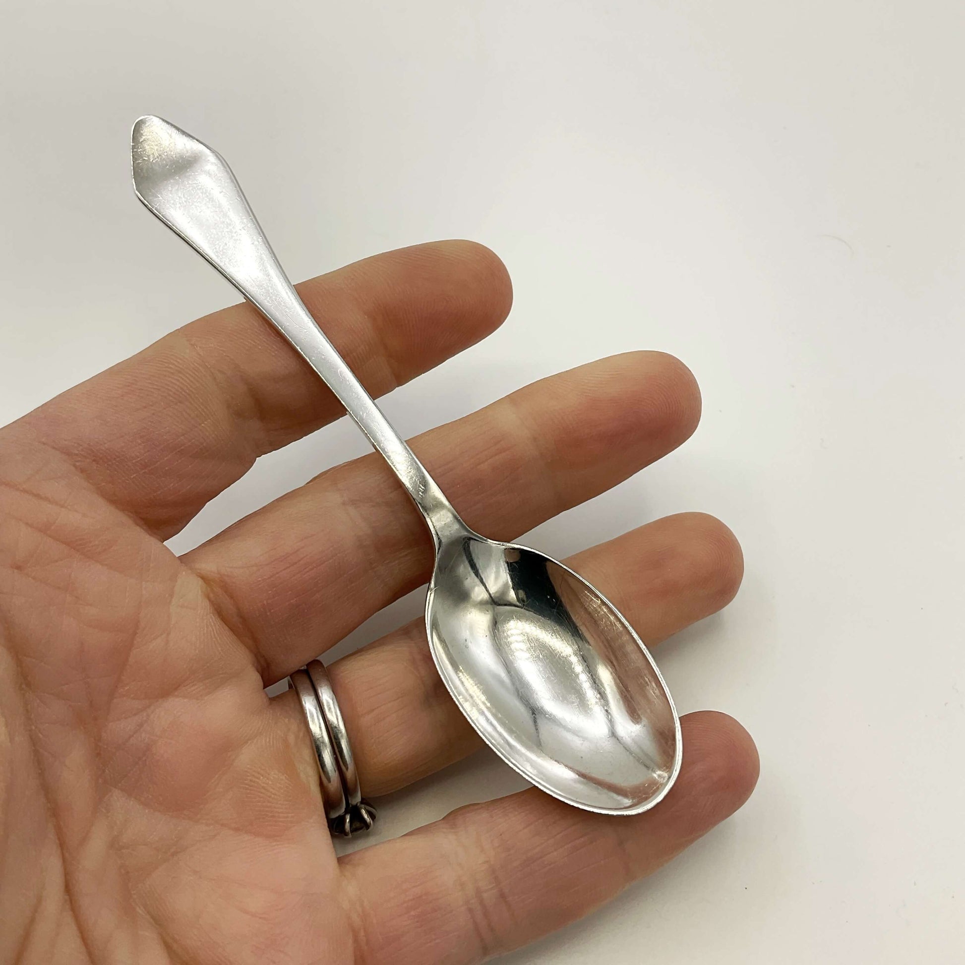 Silver coffee spoon held in a hand on a white background 
