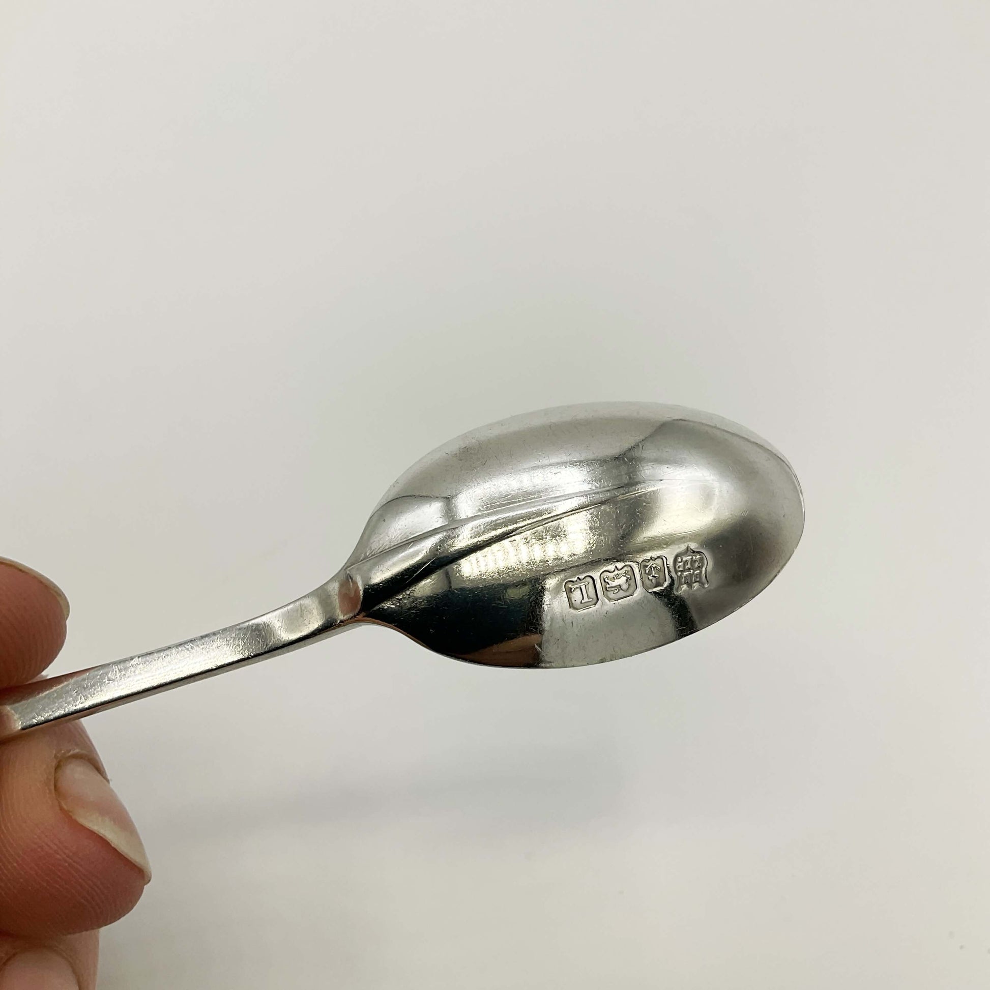 The hallmarks on the back of a coffee spoon bowl and rat tail design held in a hand with a white background 