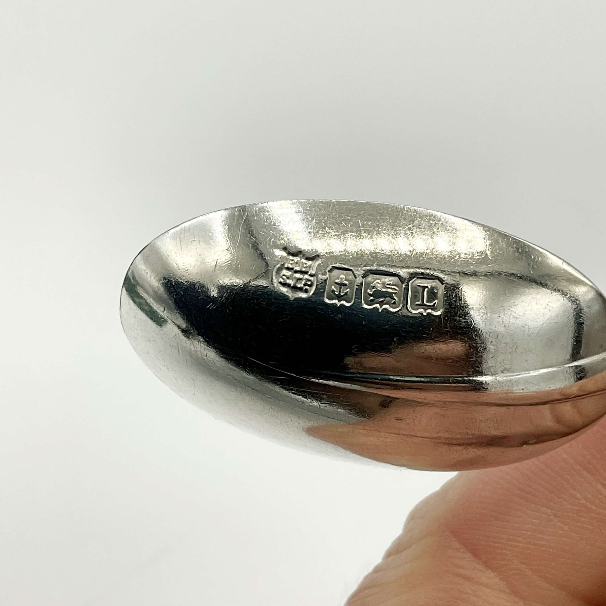 The hallmarks on the back of a coffee spoon bowl held in a hand with a white background 