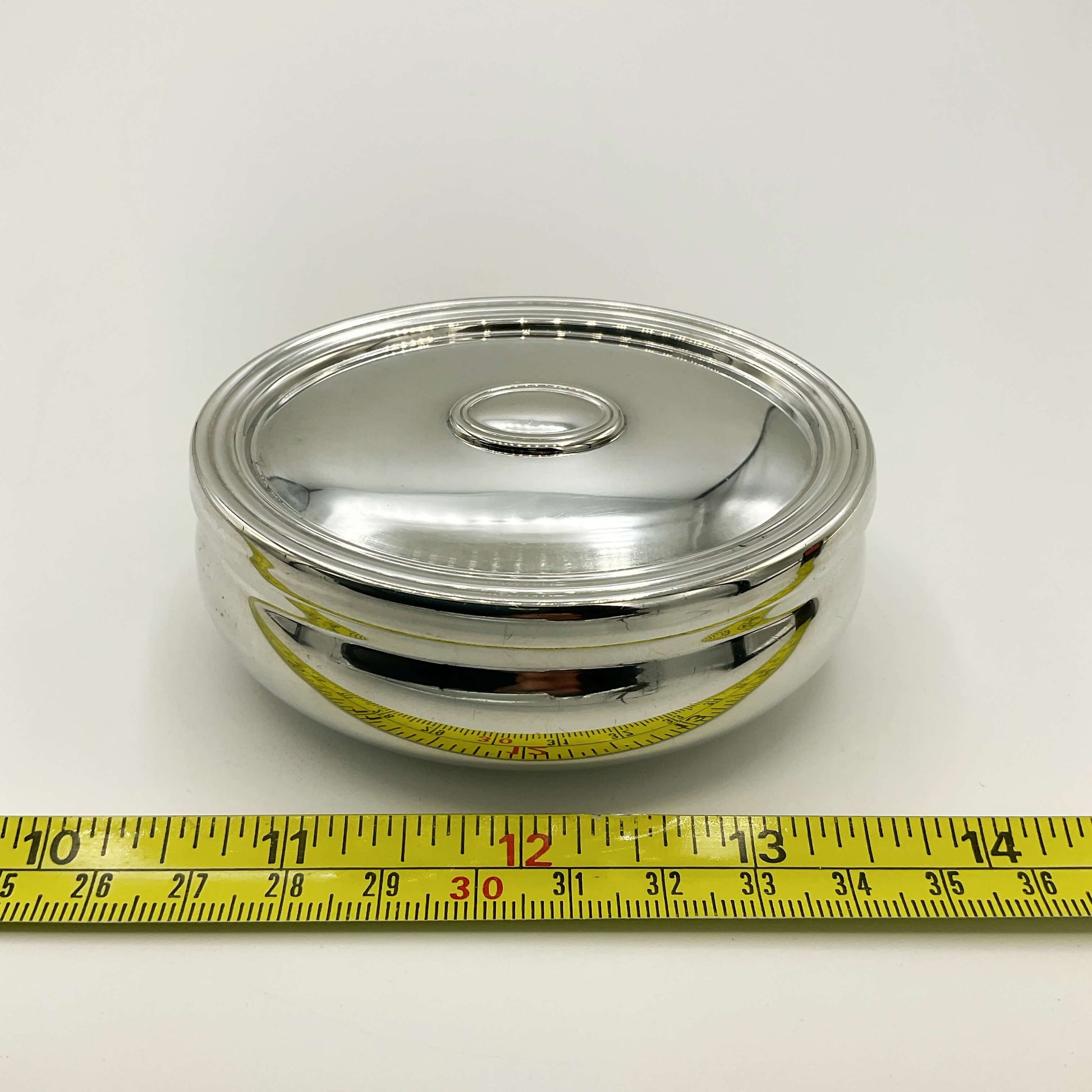 Silver trinket box on a white background next to a tape measure showing the length as 7.7cm