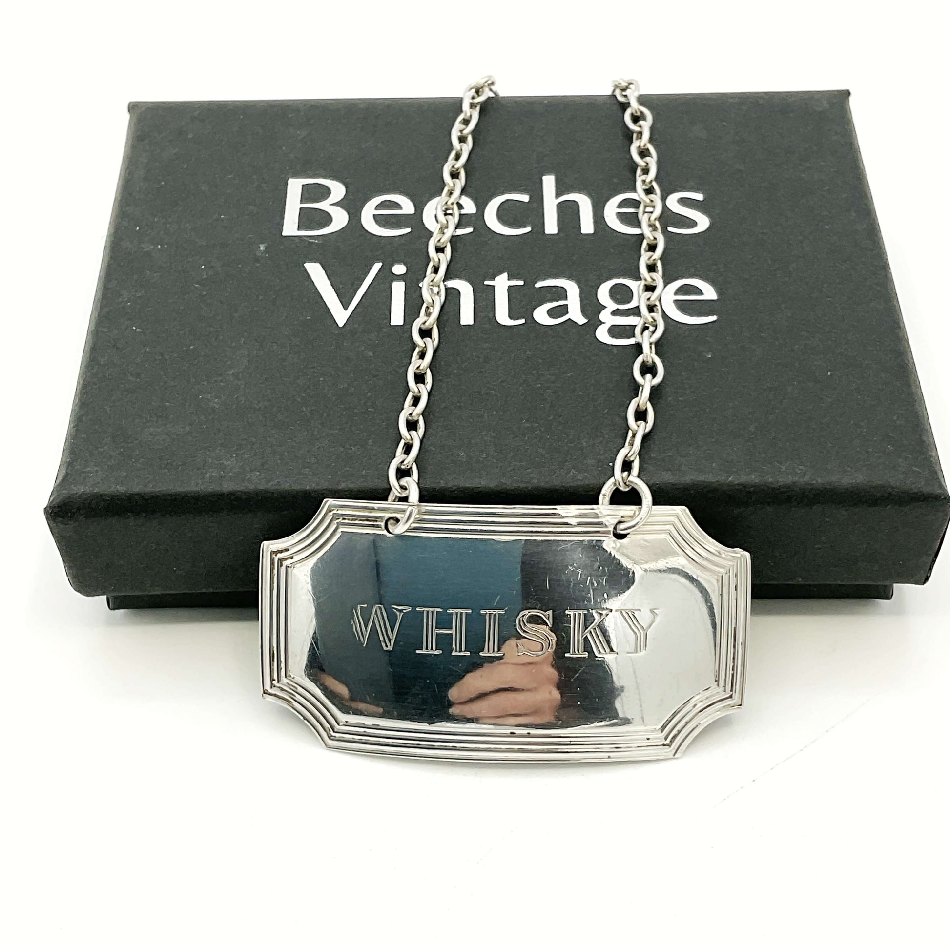 Silver Whisky decanter label in front of a black Beeches Vintage presentation box on a white background 