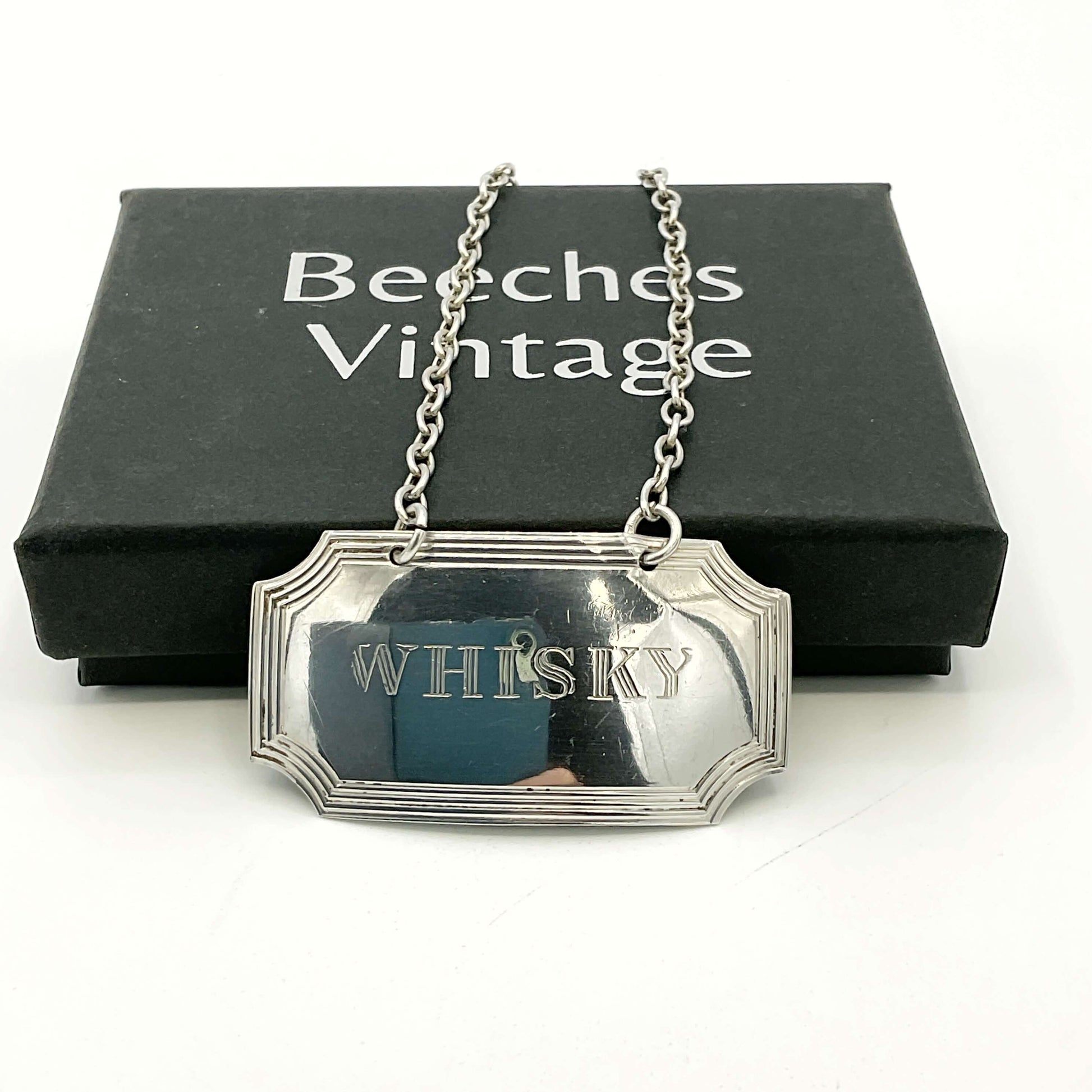 Silver Whisky decanter label in front of a black Beeches Vintage presentation box on a white background 