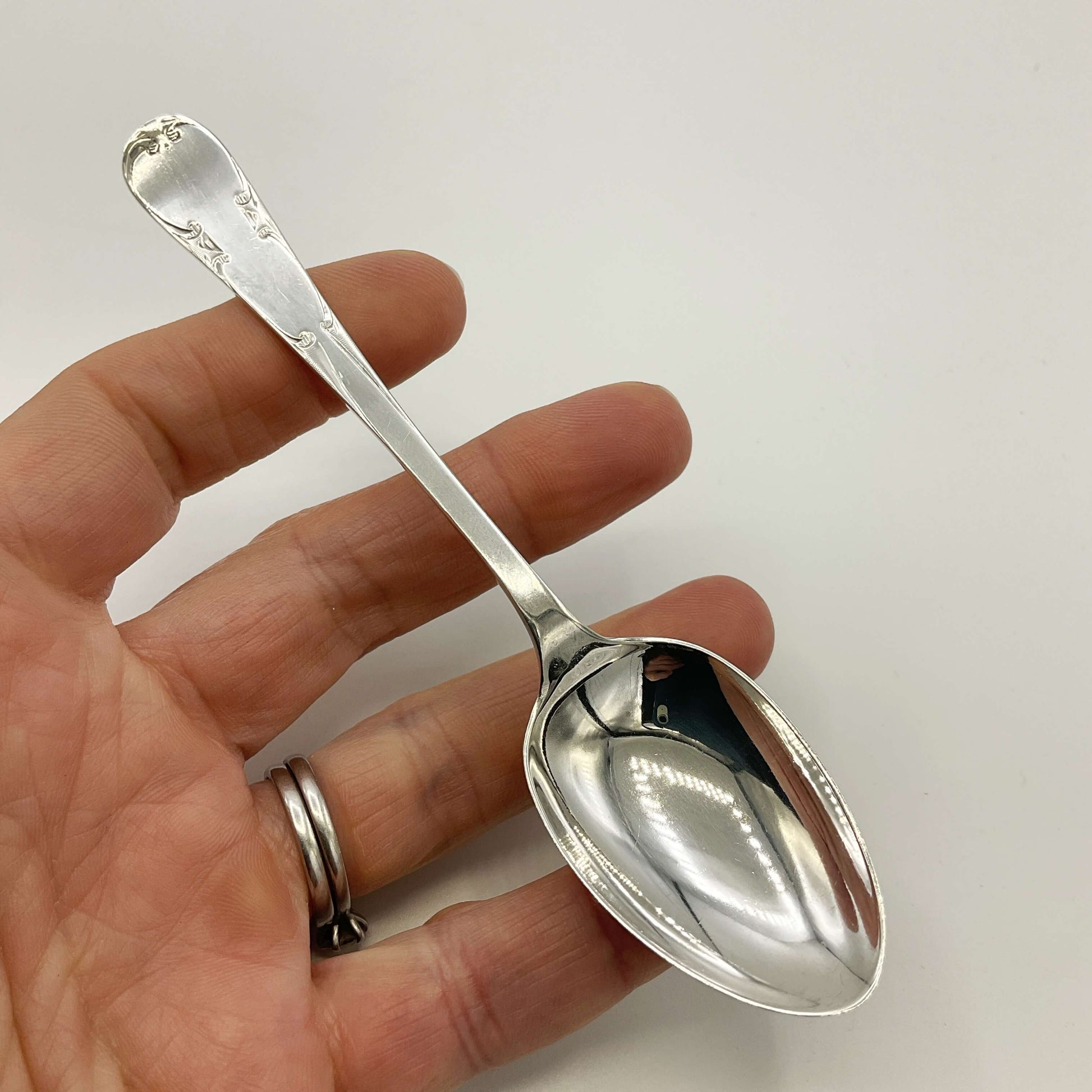 antique silver teaspoon held in a hand with a white background 