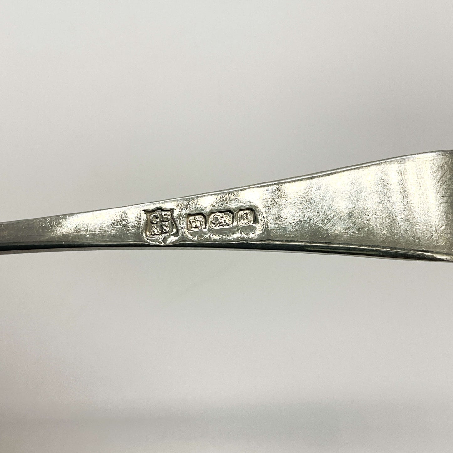 Back of Antique silver teaspoon handle showing the maker’s mark and hallmarks with a white background 