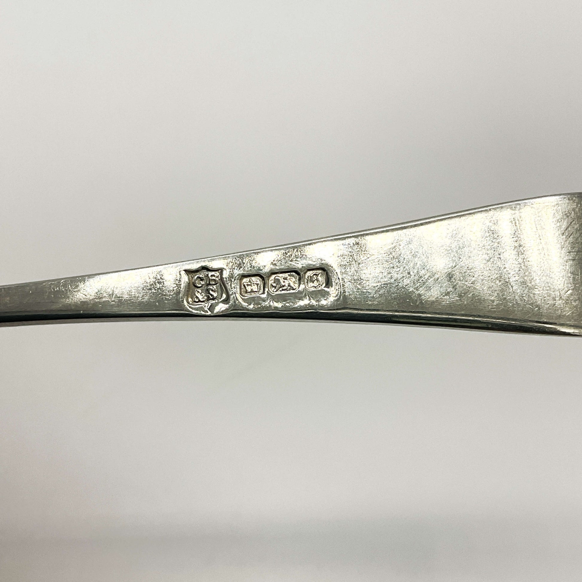 Back of Antique silver teaspoon handle showing the maker’s mark and hallmarks with a white background 