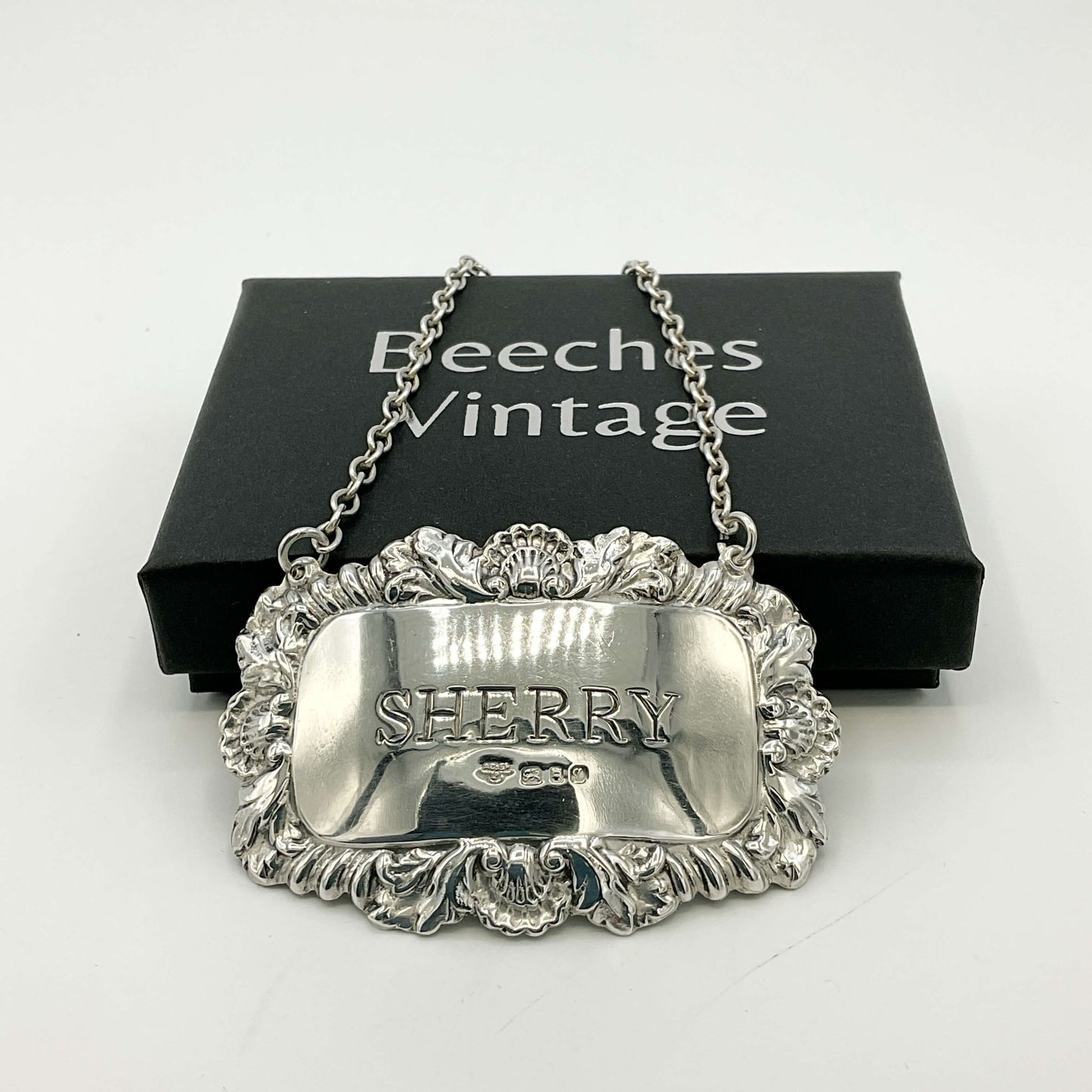 Silver Sherry decanter label in front of a black presentation box with a white background 