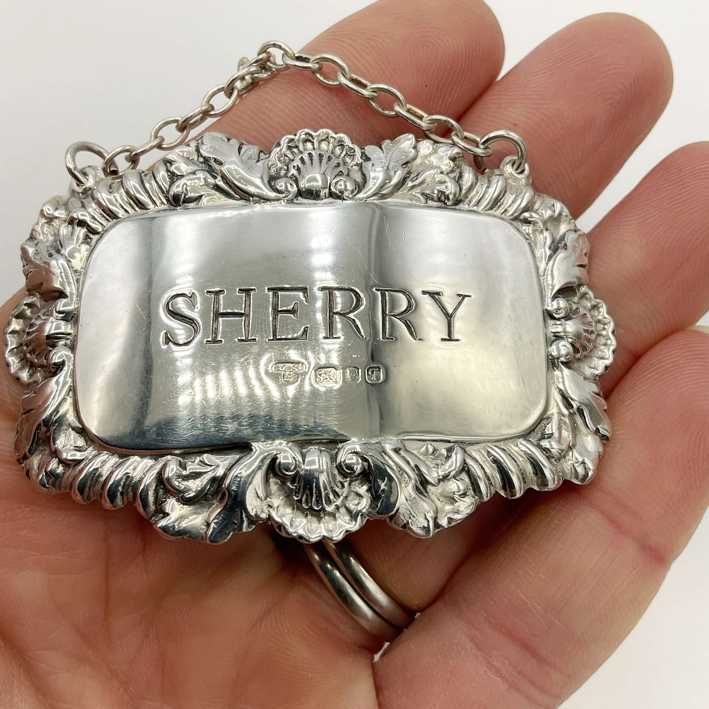 Silver Sherry decanter label held in a hand with a white background 