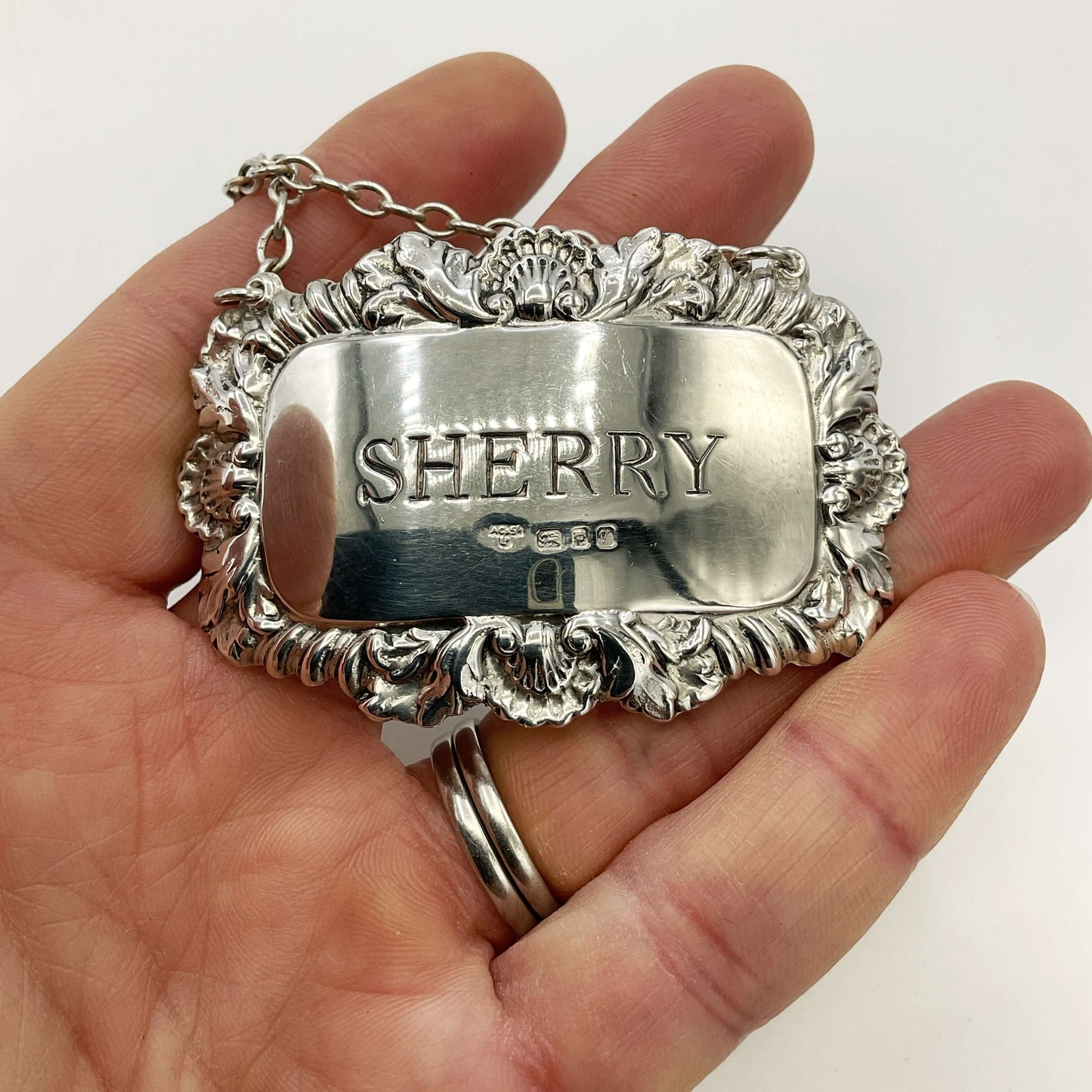 Silver Sherry decanter label held in a hand with a white background 