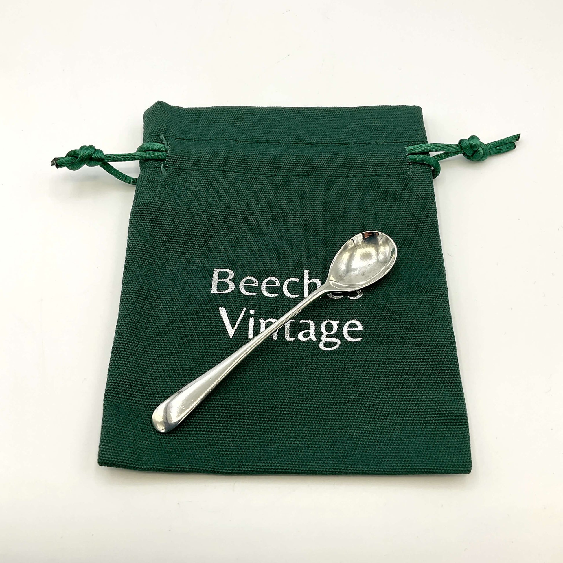 Vintage silver salt spoon on a green gift bag with a white background 