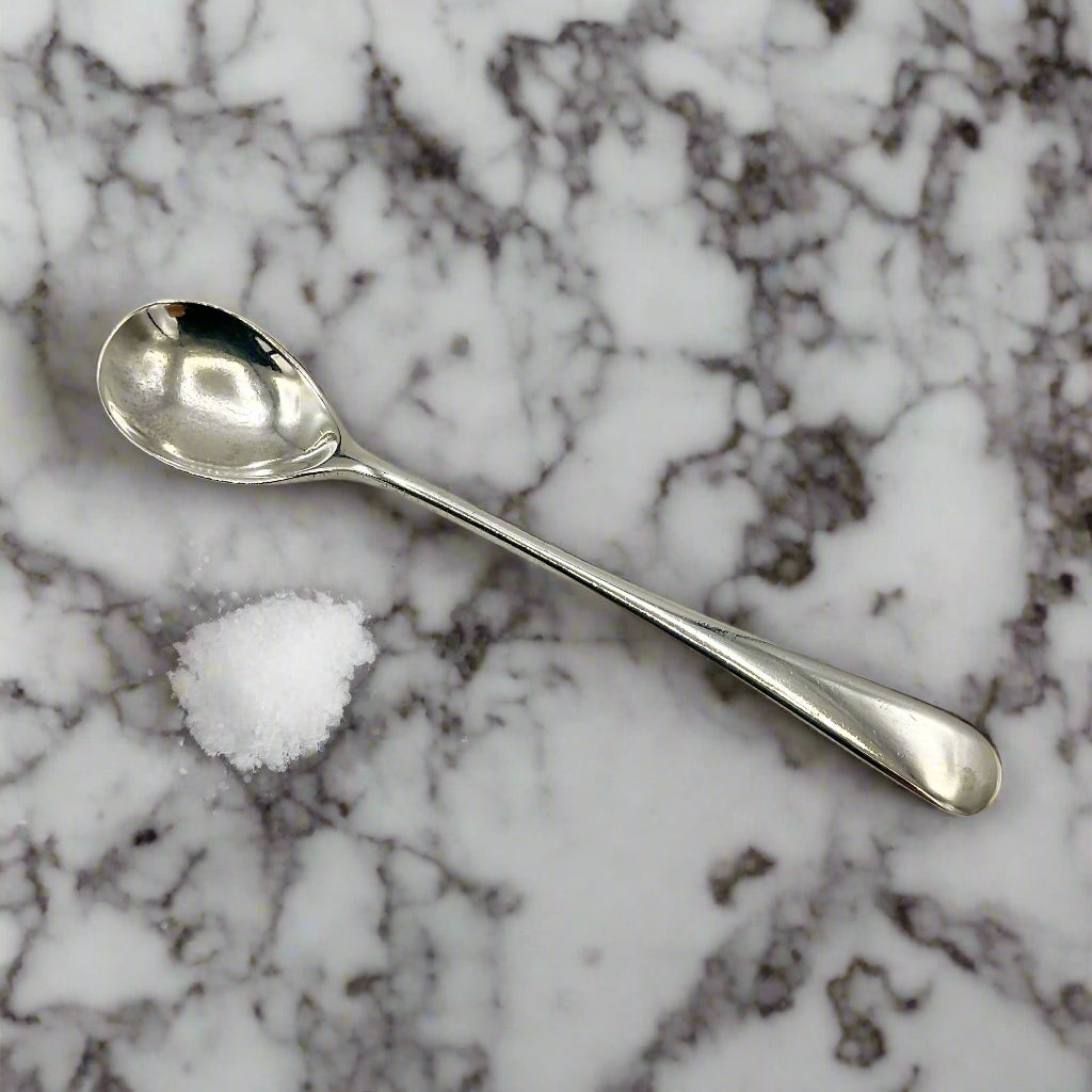 Silver salt spoon on a marble worktop next to a pile of salt