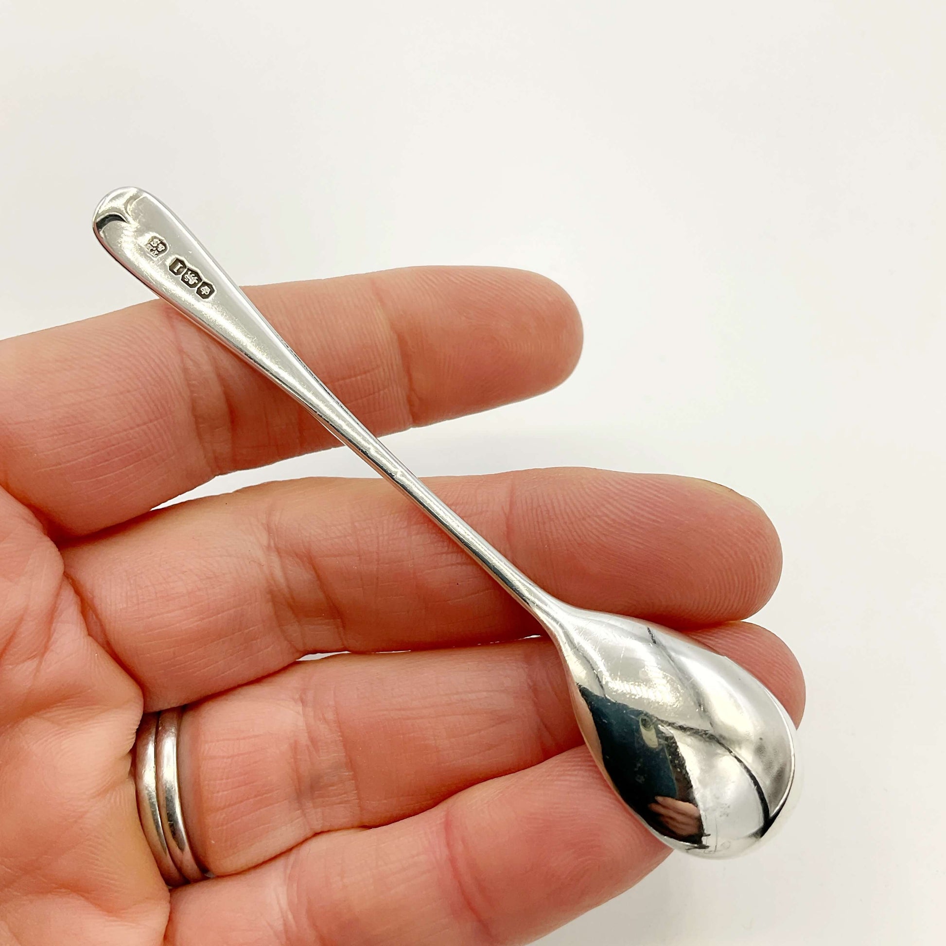 Back of silver salt spoon held in a hand with a white background 
