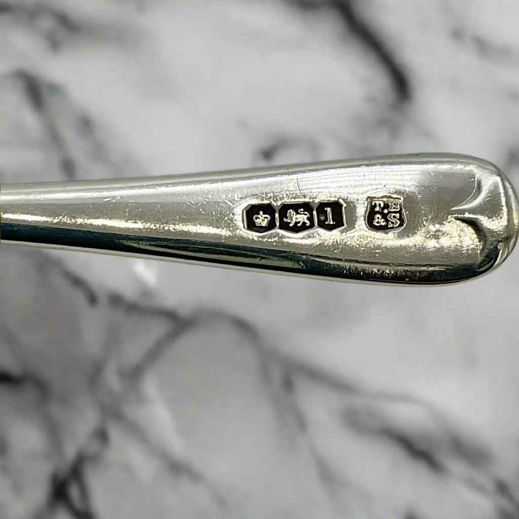 Hallmarks and makers mark on the back of a spoon handle with a marble woktop in the background 