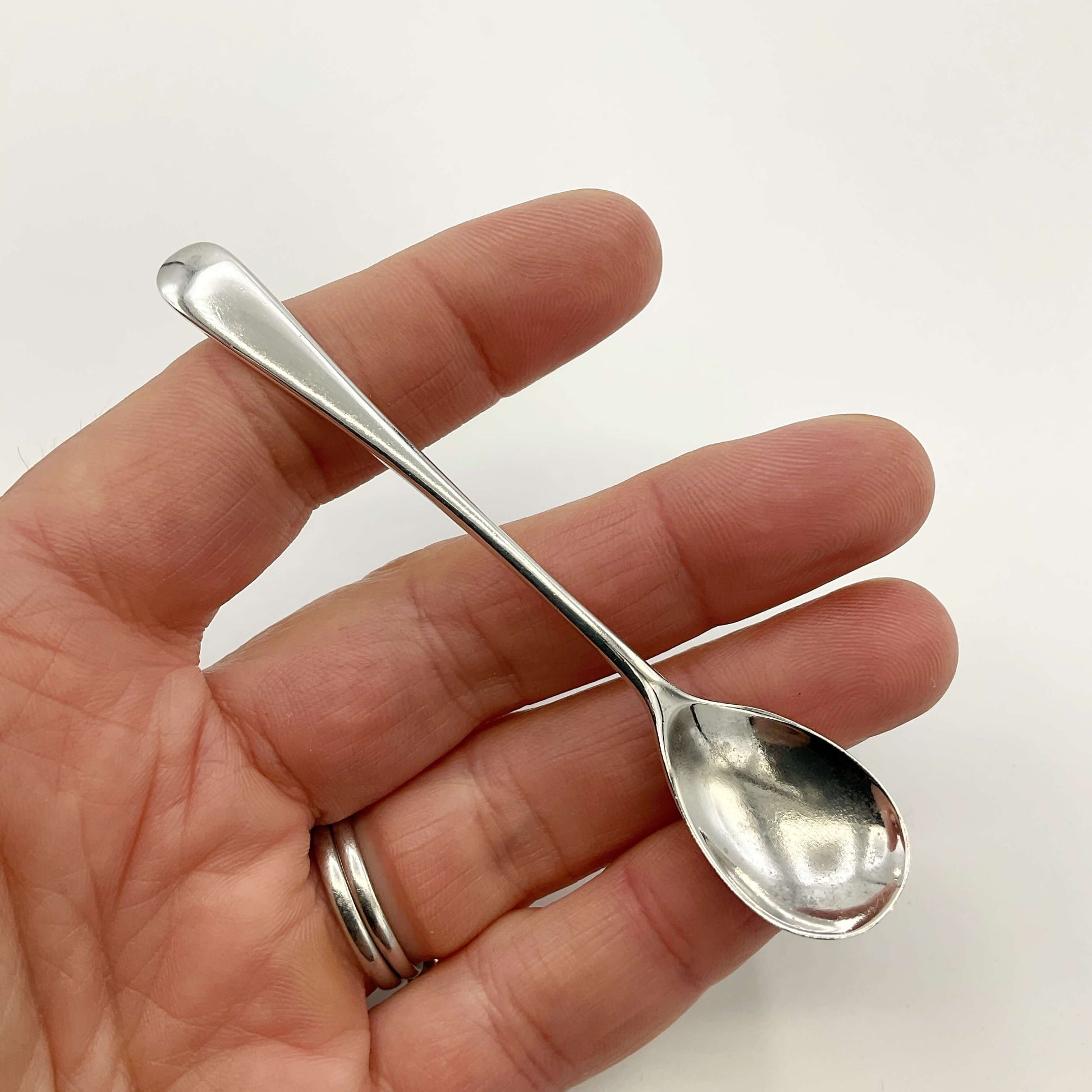 Vintage silver salt spoon held in a hand with a white background 