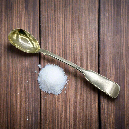 Antique silver salt spoon on a wood table next to a pile of salt